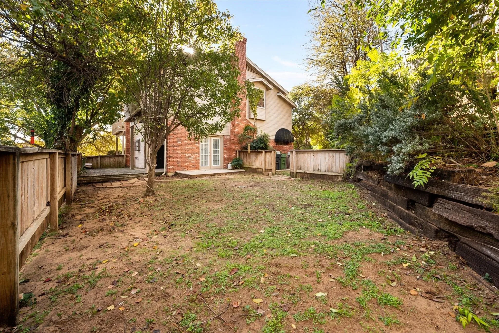 Spacious backyard featuring a wood privacy fence, a multi-tiered wood deck, and a raised planter bed with wood railroad ties