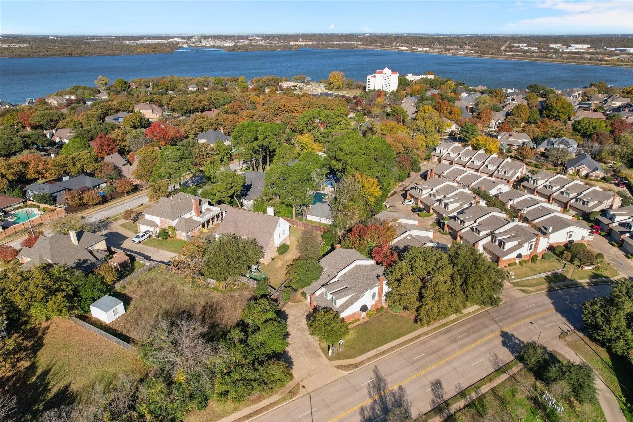 Aerial perspective showcasing a residential area with varied housing styles, mature trees, and a prominent body of water in the background