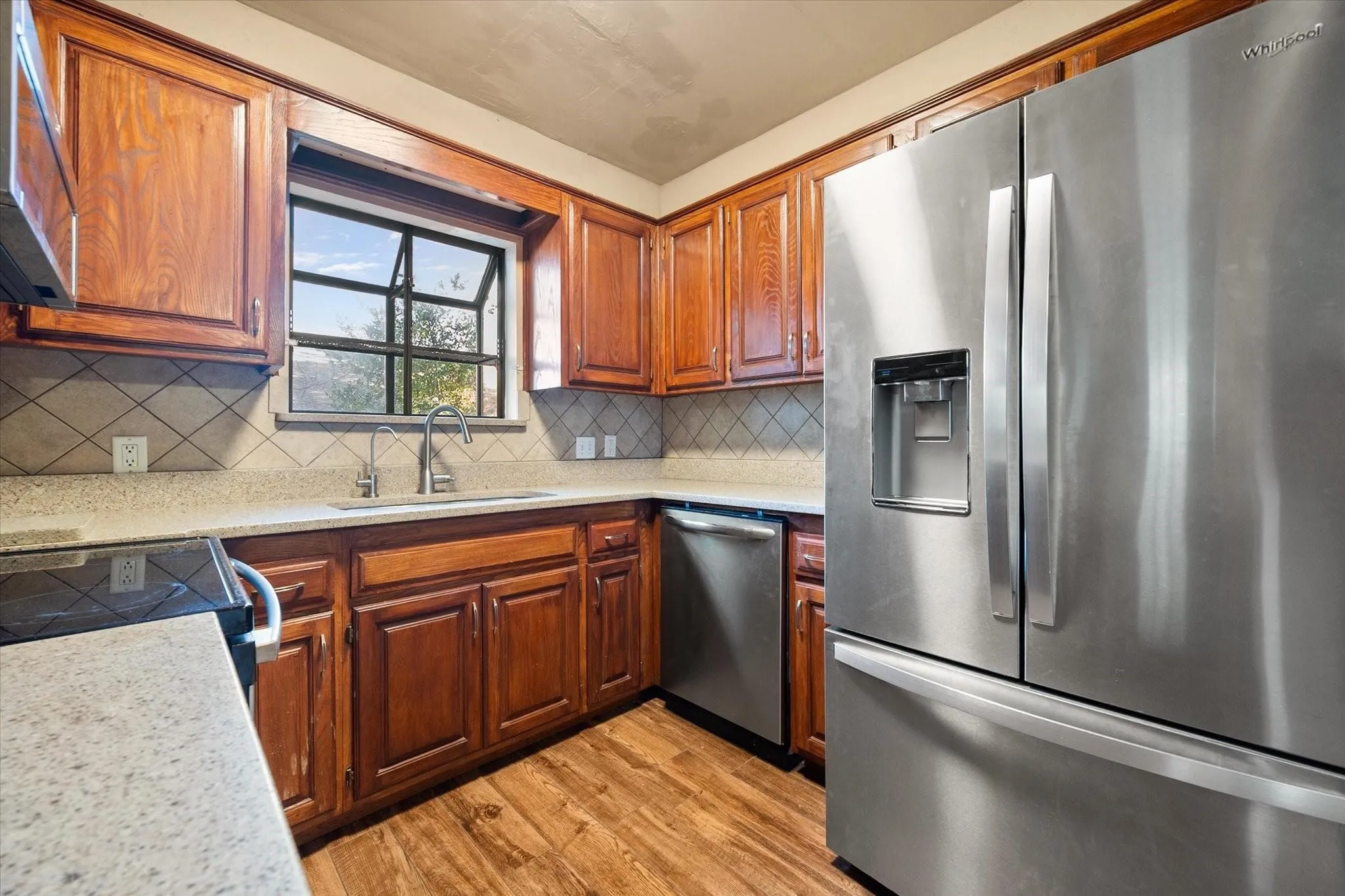 Kitchen featuring wood cabinetry, light-toned countertops, a stainless steel over-the-range microwave, and a black and stainless steel electric range