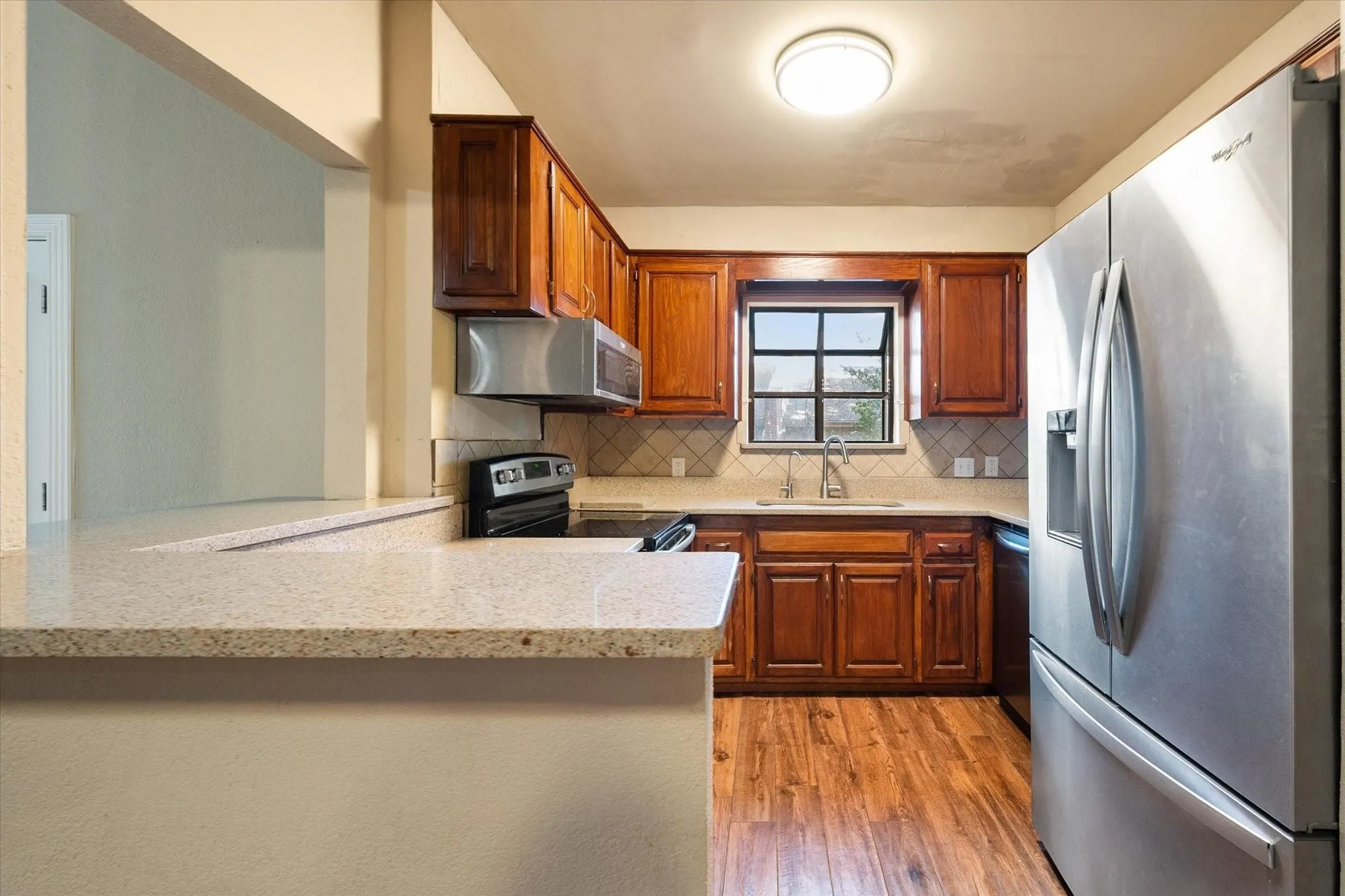 Kitchen featuring wood-finish flooring, warm-toned cabinetry, stainless steel appliances, a tile backsplash, and a breakfast bar