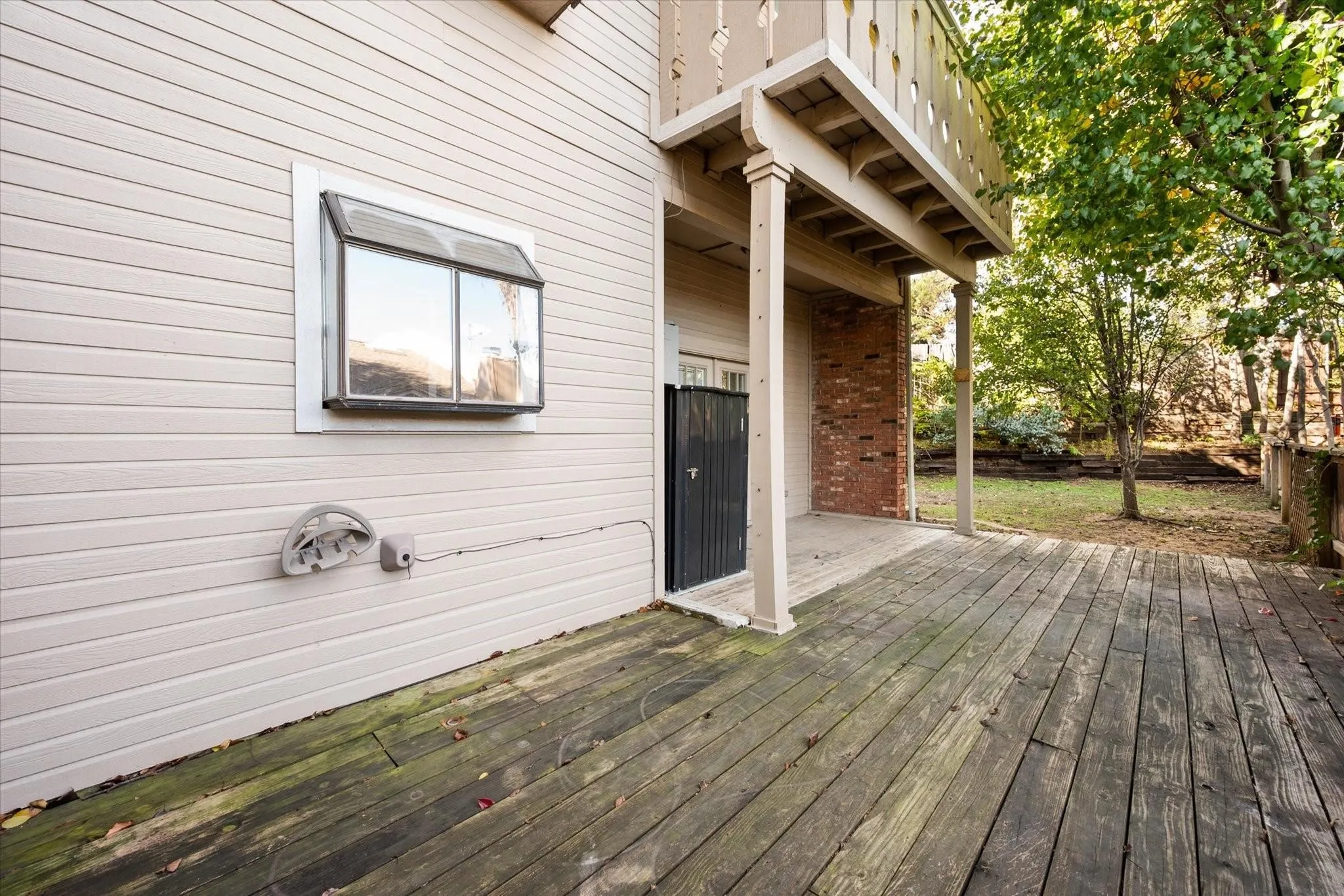 Outdoor wood deck with a partial overhead covering, featuring a wood privacy fence and mature trees