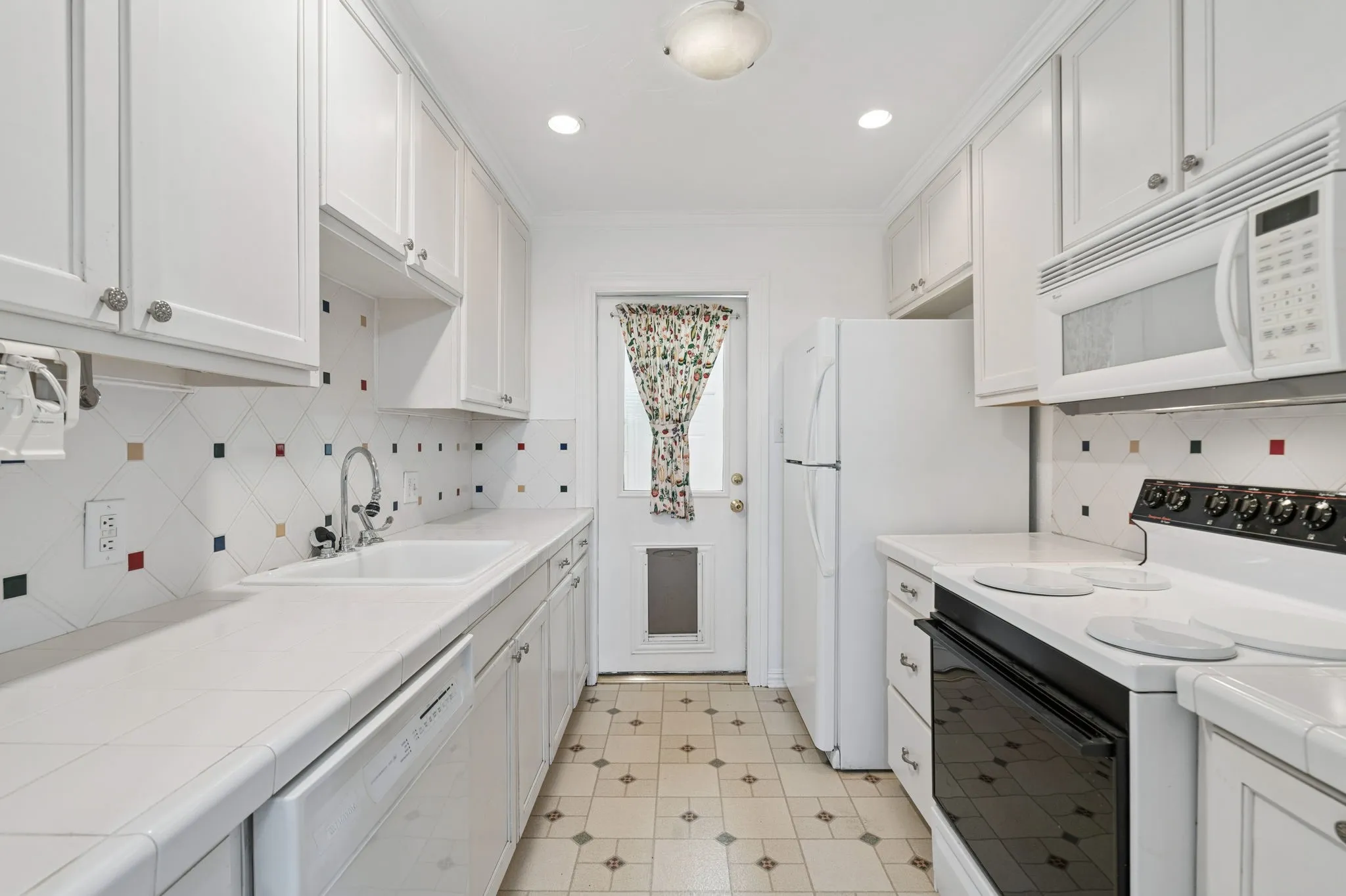 Galley kitchen featuring white cabinetry, integrated white appliances, and a mosaic tile backsplash