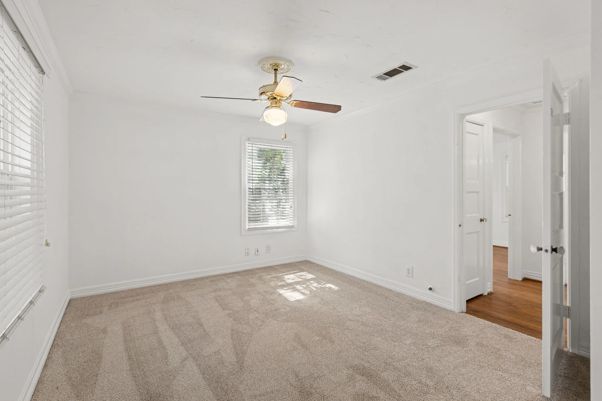 Neutral tone bedroom featuring two windows with horizontal blinds, a ceiling fan with integrated lighting, crown molding, and carpet flooring