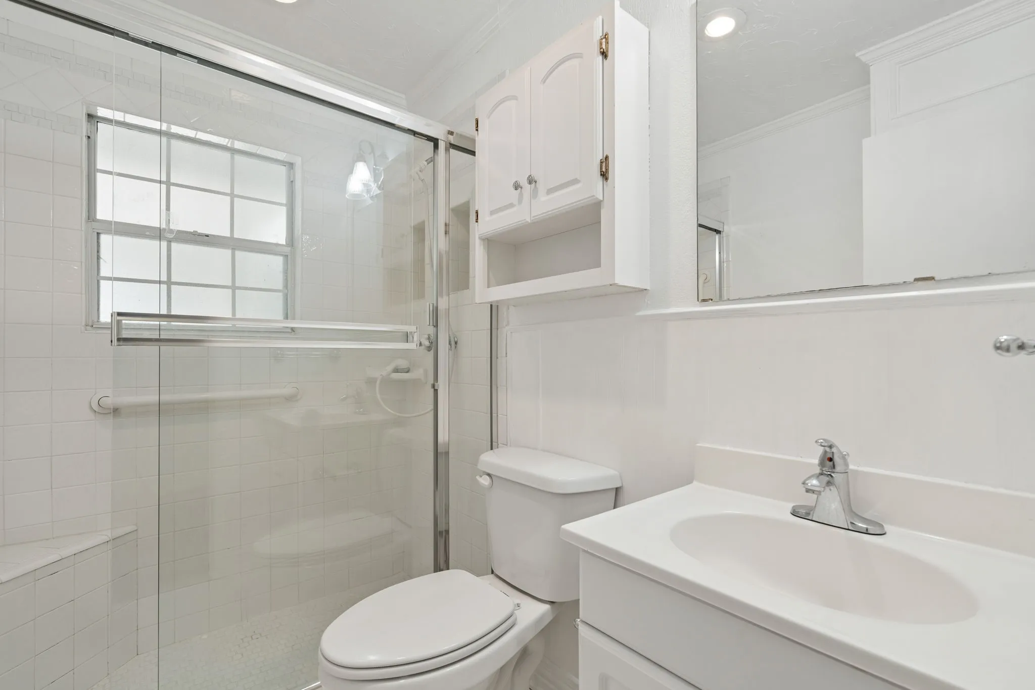 Bathroom featuring a single vanity, a chrome faucet, a wall-mounted mirror, and a built-in shower with a window