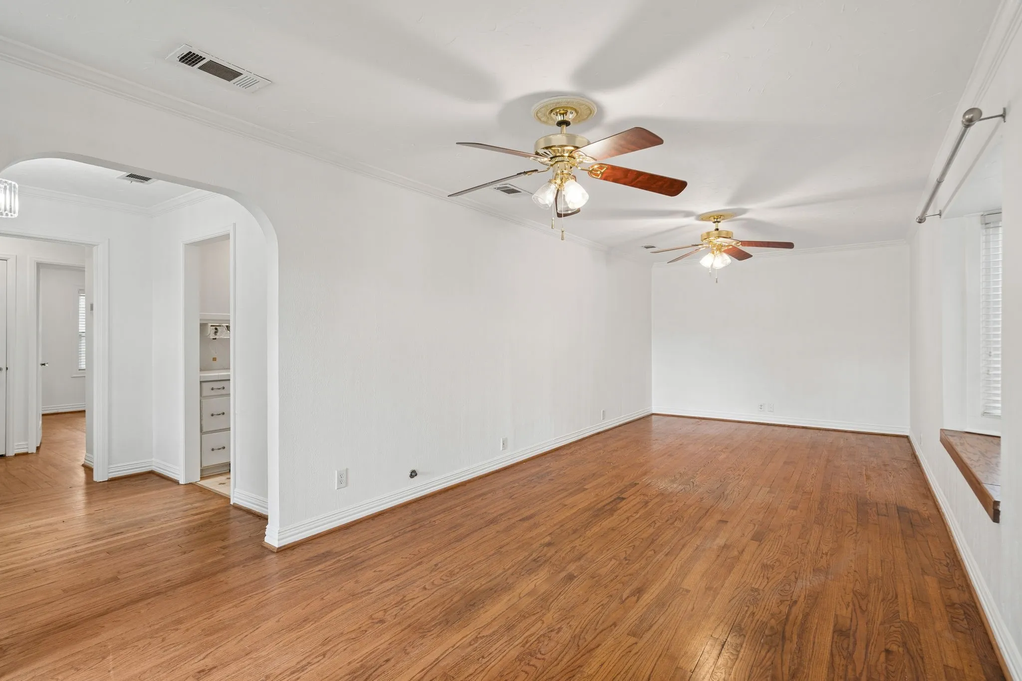 Spacious interior room featuring wood-finish flooring, white walls, and elegant crown molding