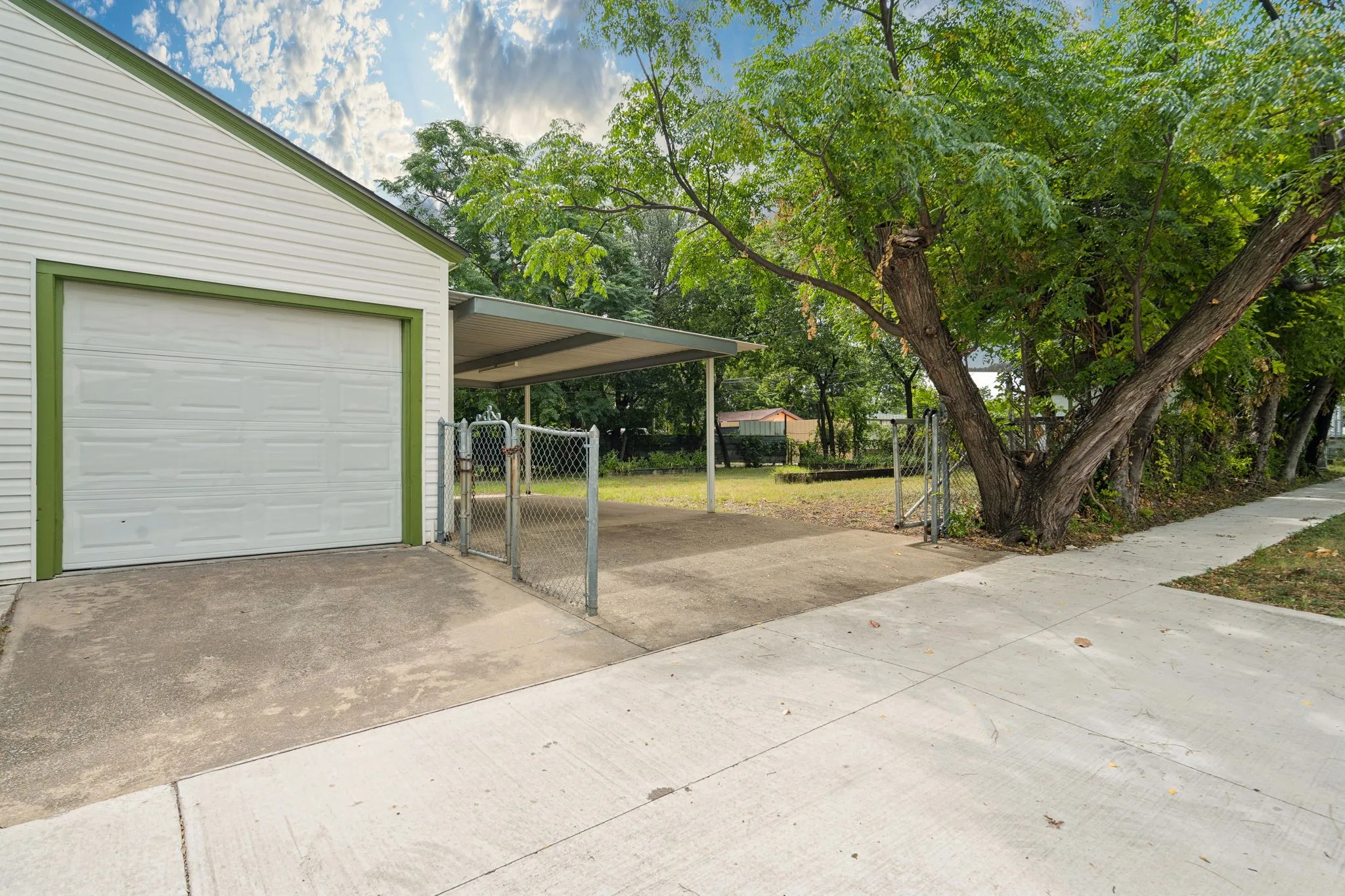 Attached single-car garage with white paneled door and green trim with gated access to back yard and side covered parking area.