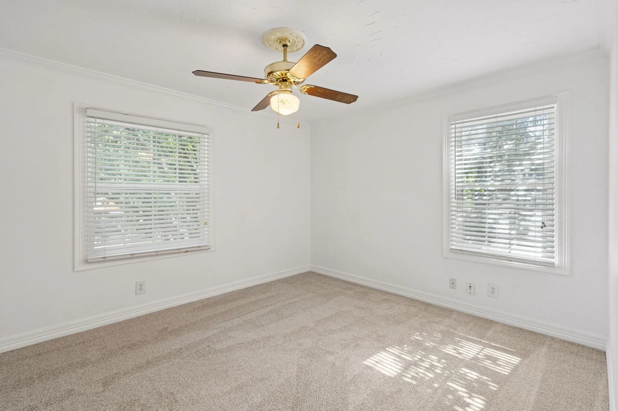 Neutral tone bedroom featuring two windows with horizontal blinds, a ceiling fan with integrated lighting, crown molding, and carpet flooring
