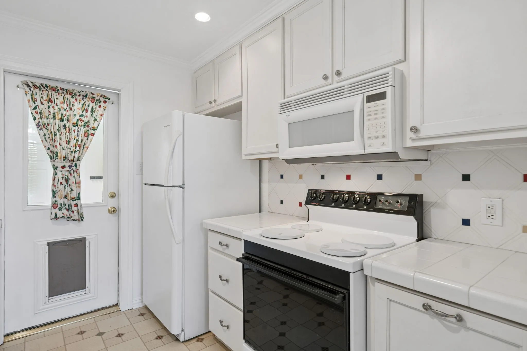 Kitchen featuring white cabinetry with brushed nickel hardware, white tile countertops, and a white tile backsplash with colorful accent squares