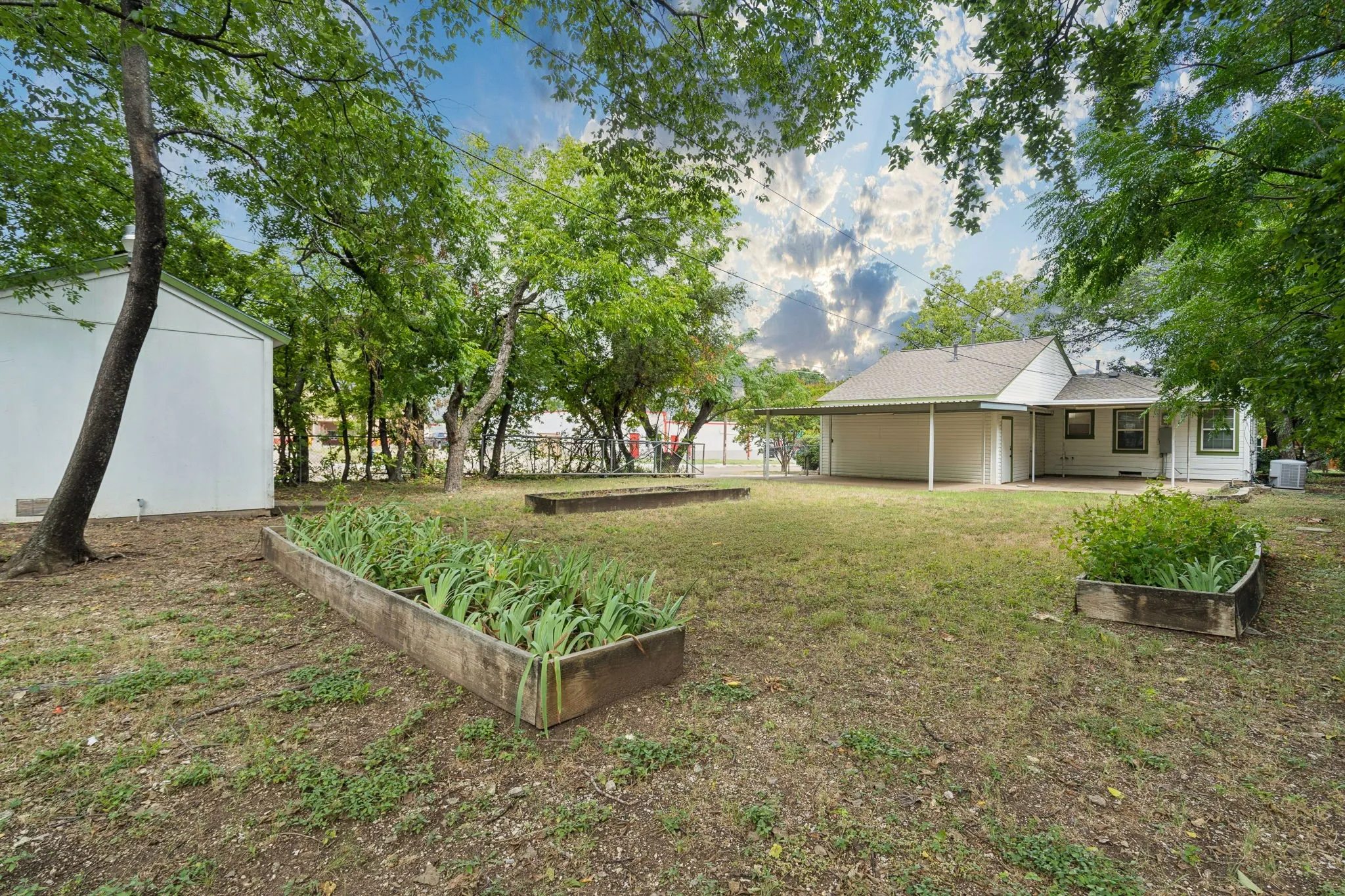 Expansive backyard featuring a storage shed, mature trees, raised garden beds, and a covered patio
