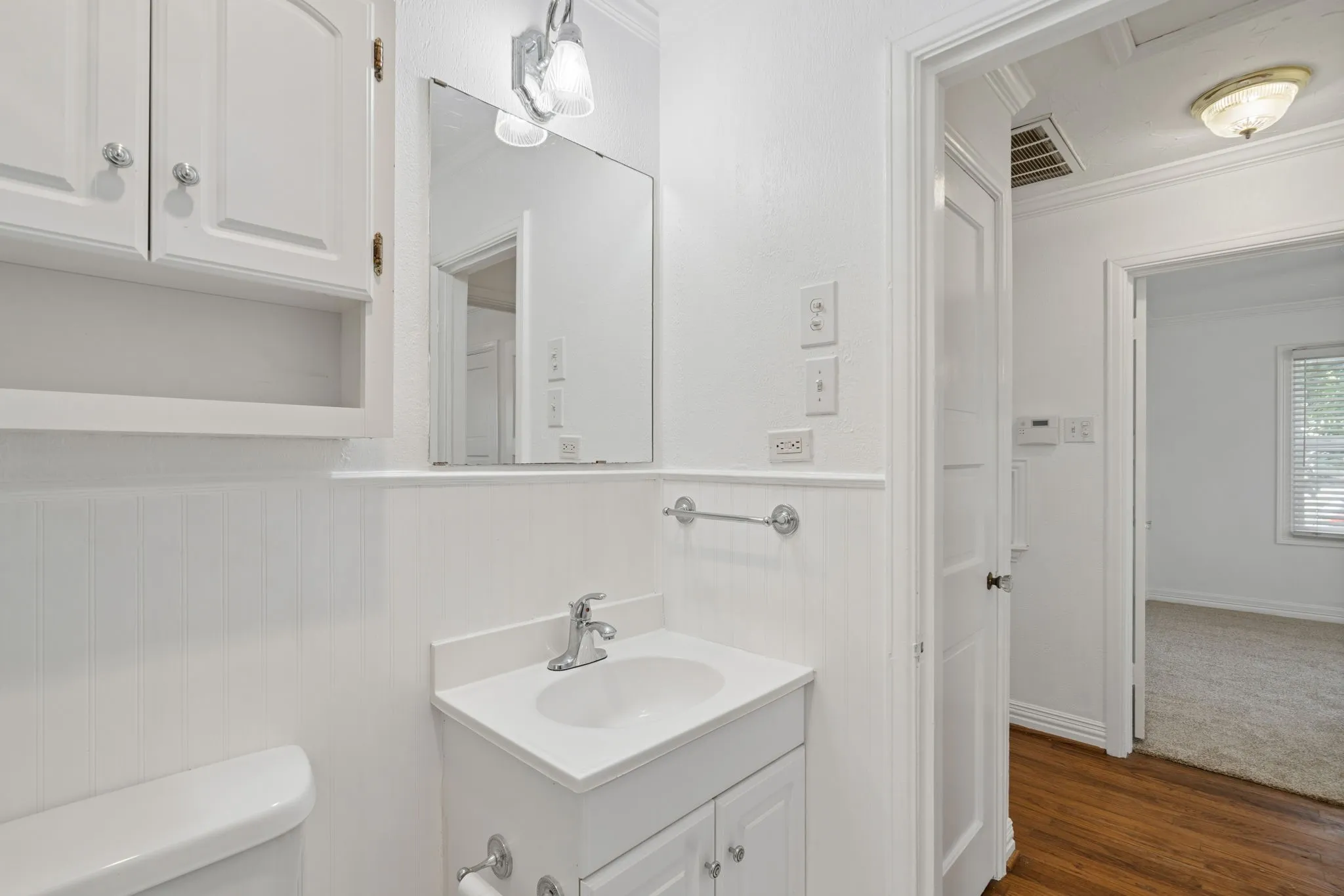 White vanity with integrated sink, chrome faucet, and mirrored medicine cabinet