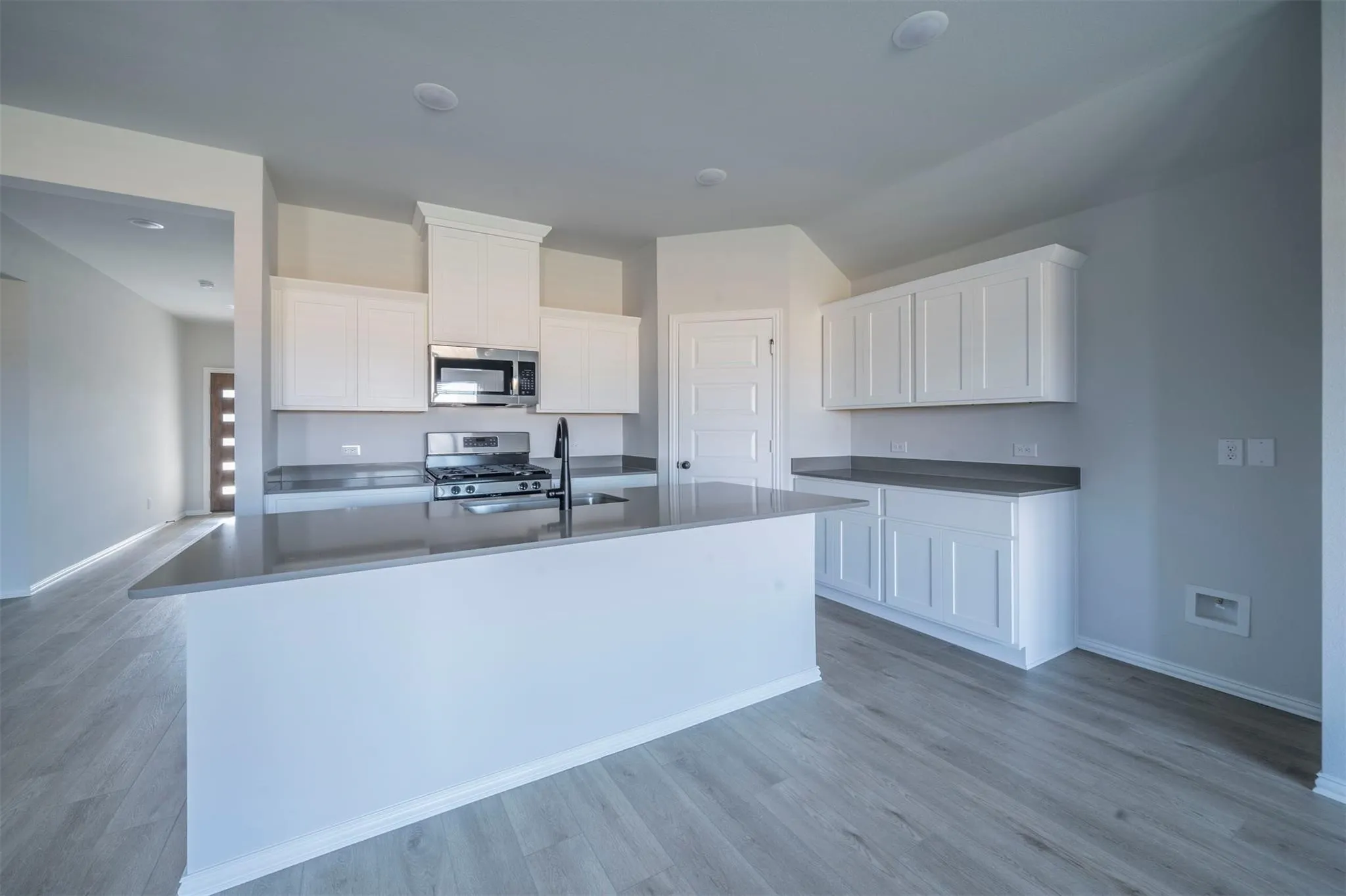 Kitchen featuring a center island, white cabinetry, integrated stainless steel appliances, and wood-finish flooring