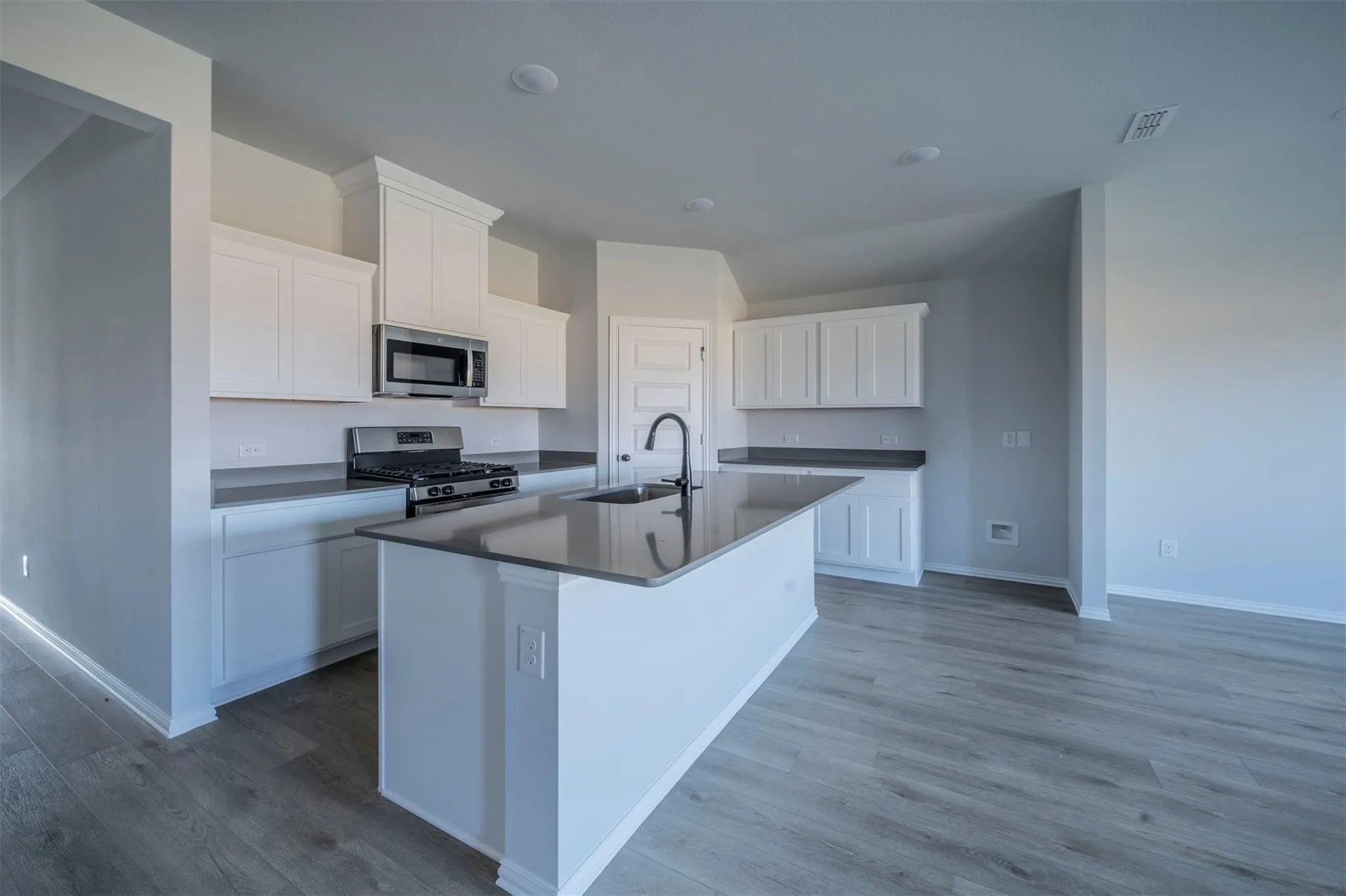 Contemporary kitchen featuring an island with a sink, white cabinetry, dark countertops, stainless steel appliances, and wood-finish flooring
