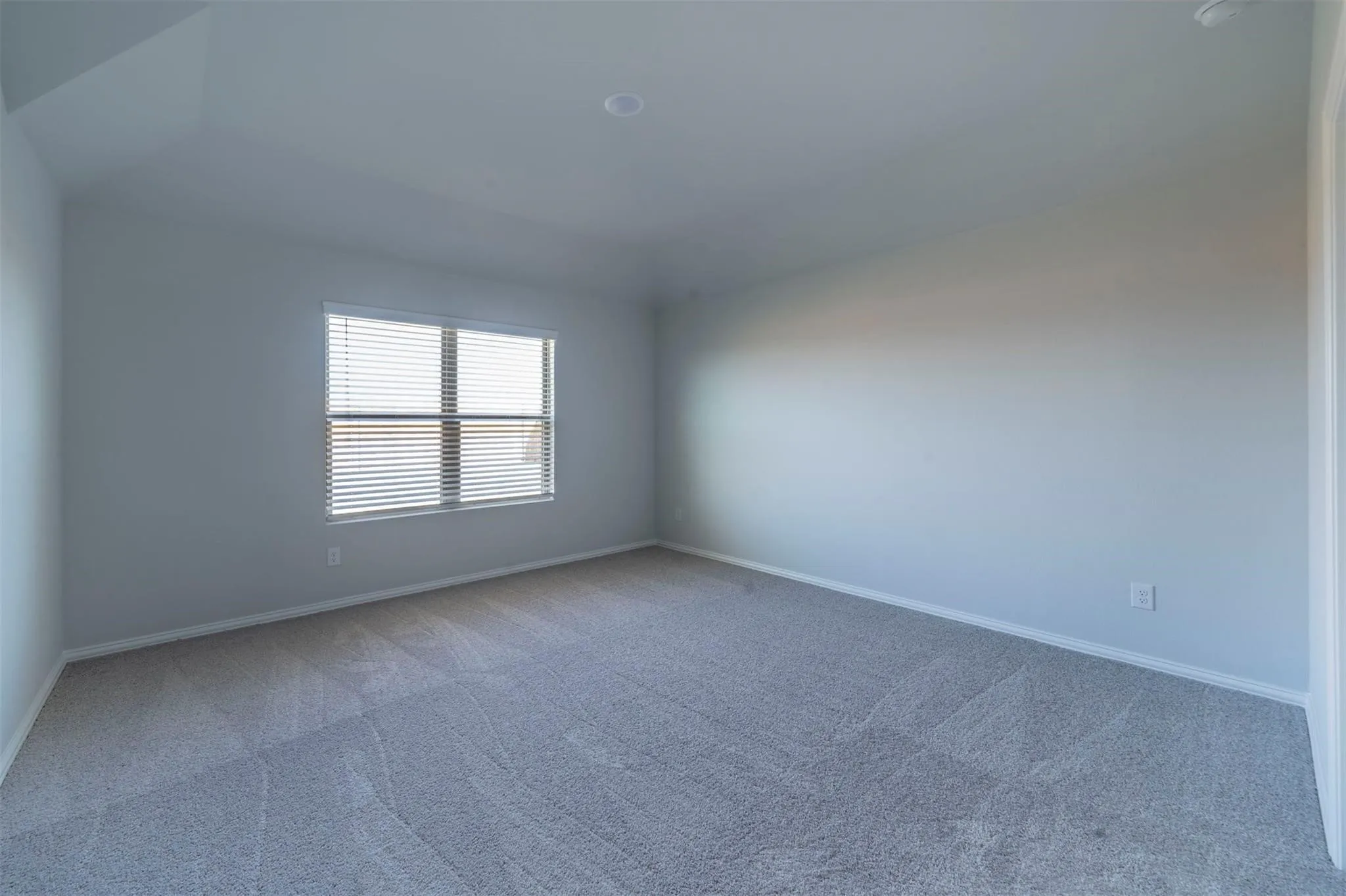 Carpeted room featuring a single window with horizontal blinds, white baseboards, and a recessed ceiling light