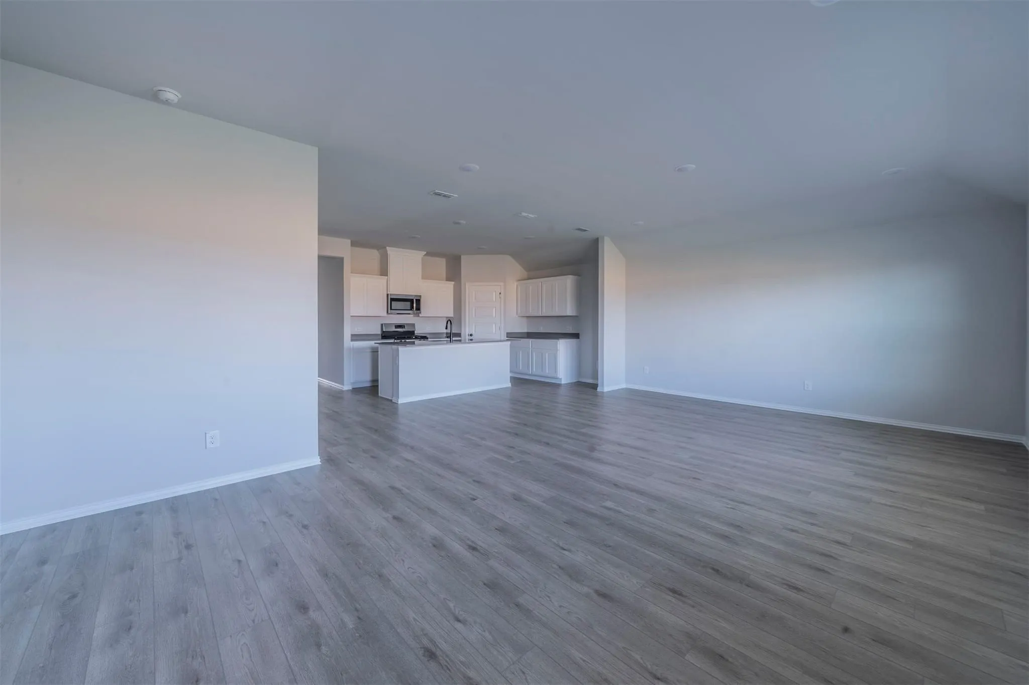 Spacious room with wood-finish flooring, light grey walls, and recessed lighting