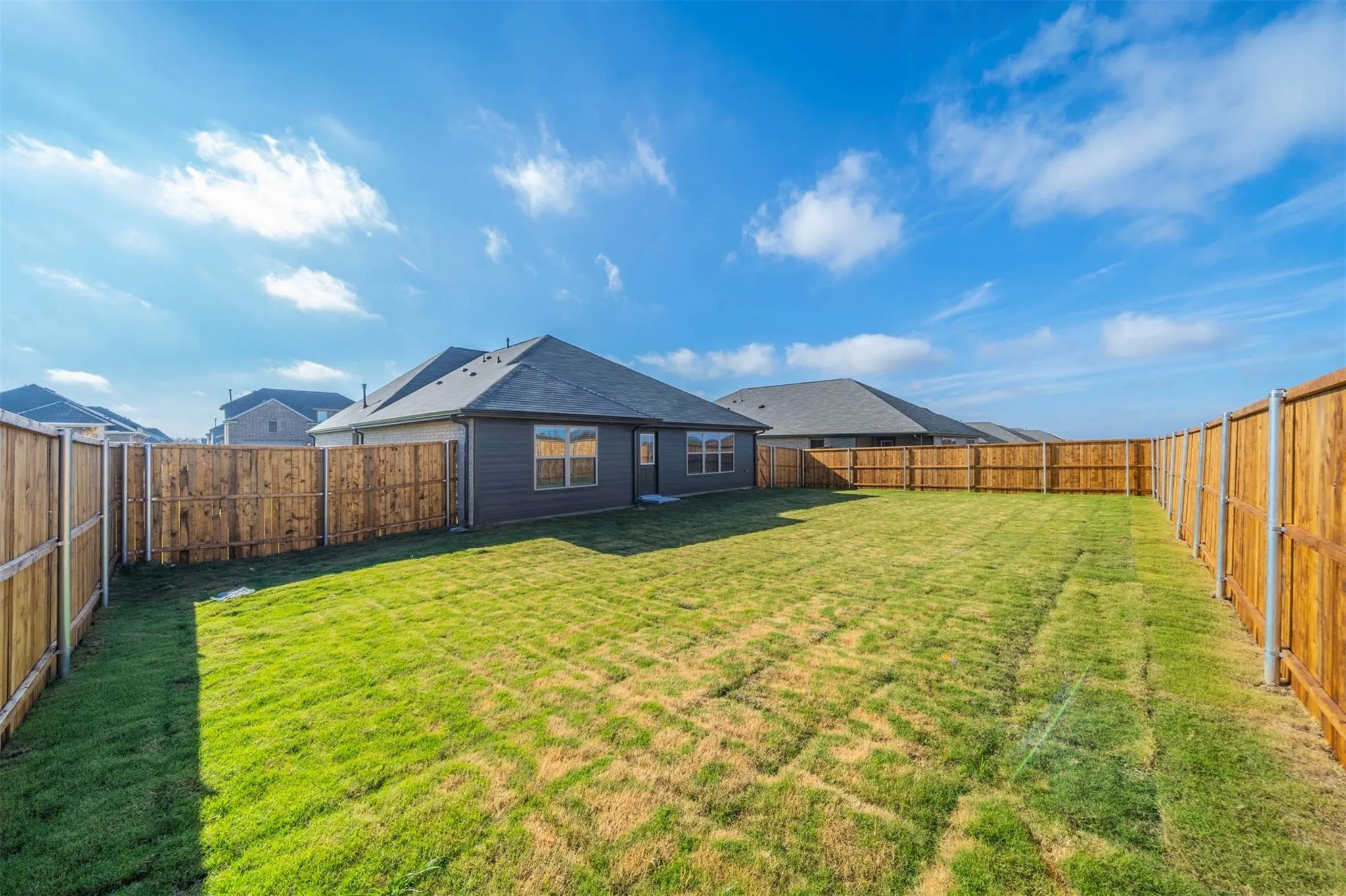 Expansive backyard featuring a manicured lawn, full privacy fencing, and a contemporary single-story residence with a dark gray exterior and multiple windows