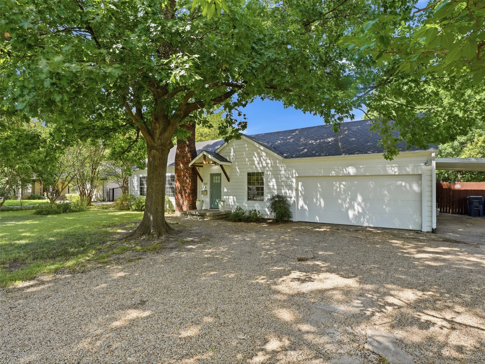 White exterior residence featuring a front gravel driveway and a mature shade tree
