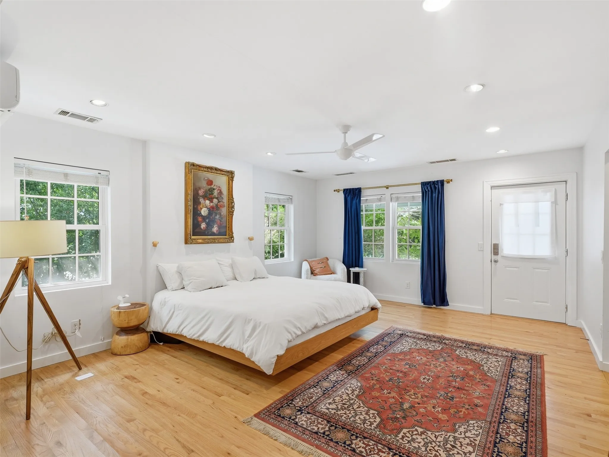 Bright bedroom featuring light wood-finish flooring and multiple windows with white blinds