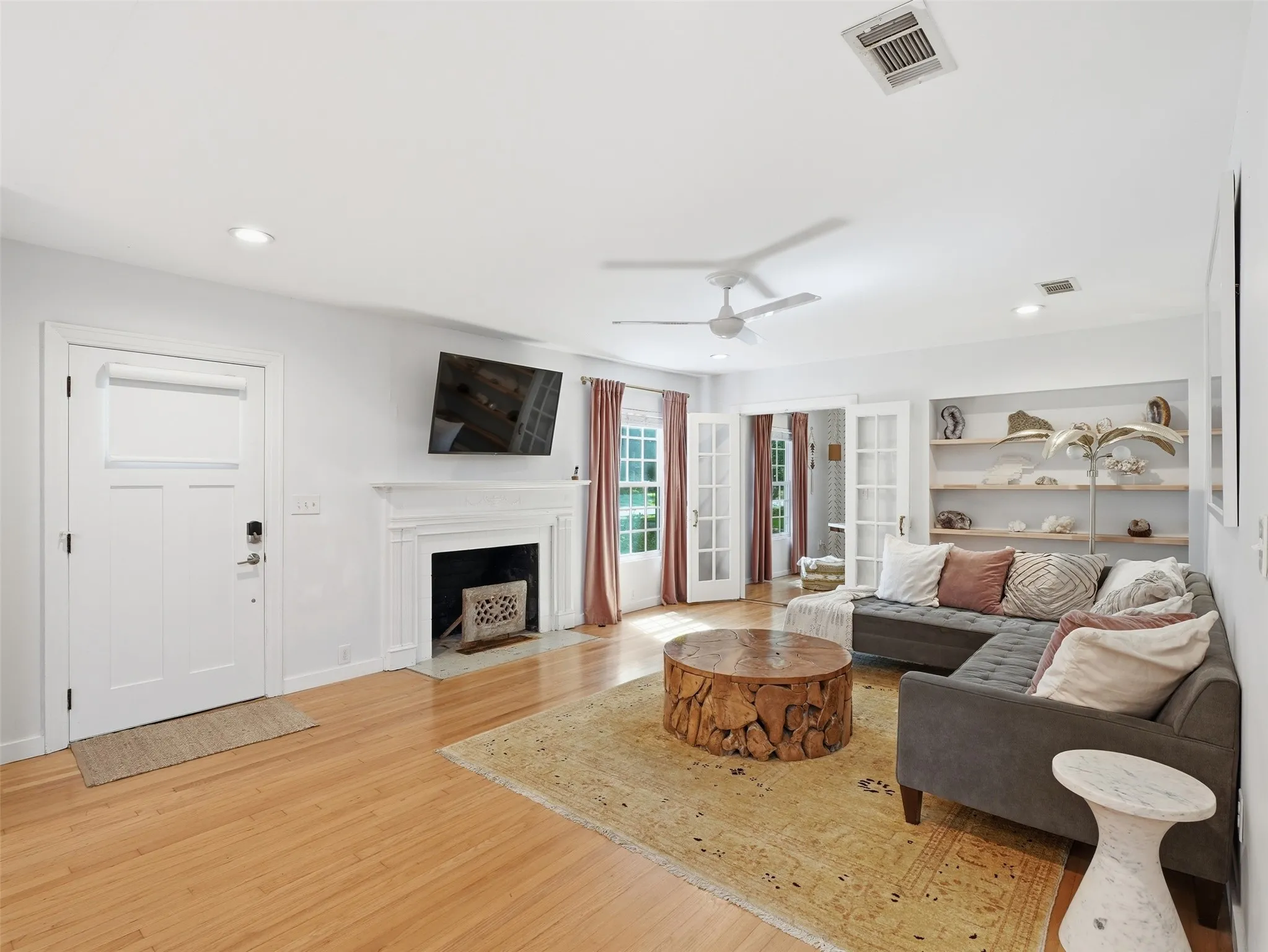 Living room featuring wood-finish flooring, a fireplace with a white mantel, and built-in shelving