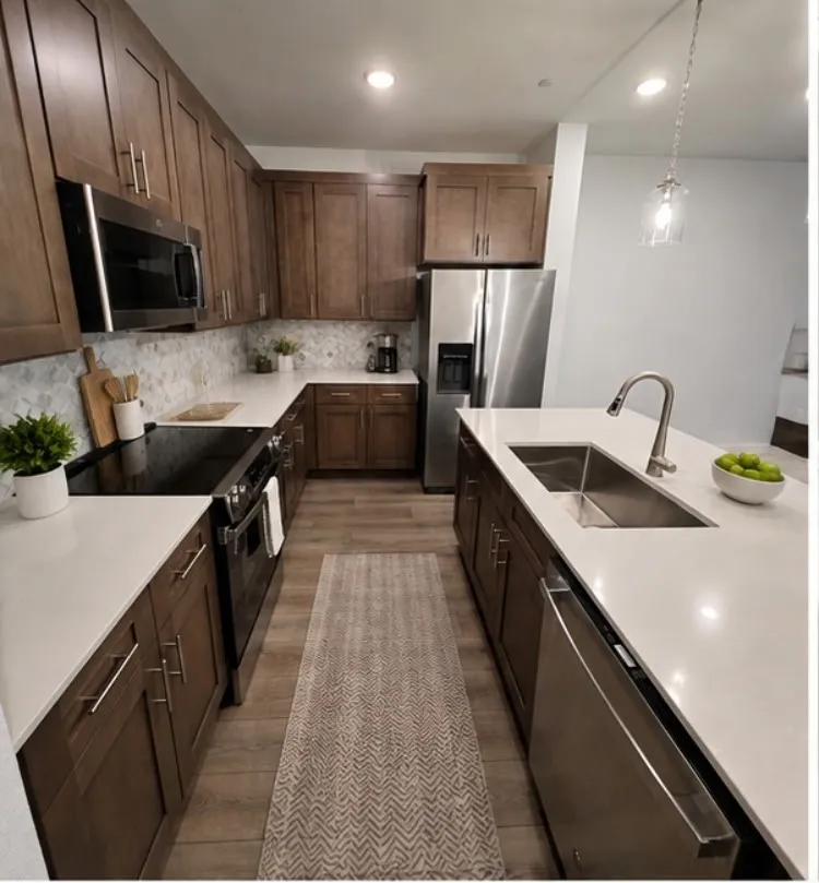 Modern kitchen featuring rich wood cabinetry, stainless steel appliances, white countertops, and a patterned tile backsplash