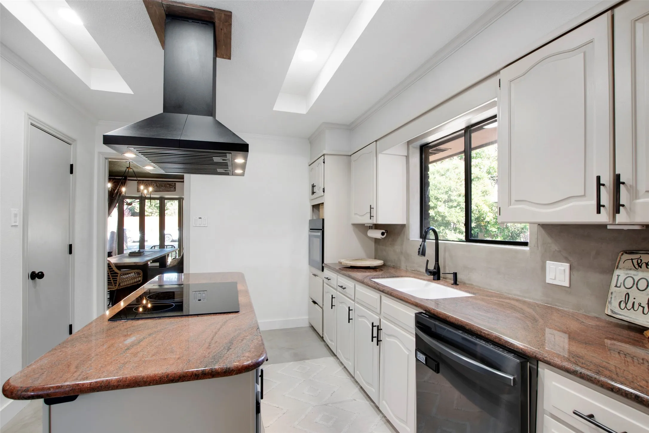 Kitchen with stainless steel appliances, decorative backsplash, sink, island exhaust hood, and white cabinetry