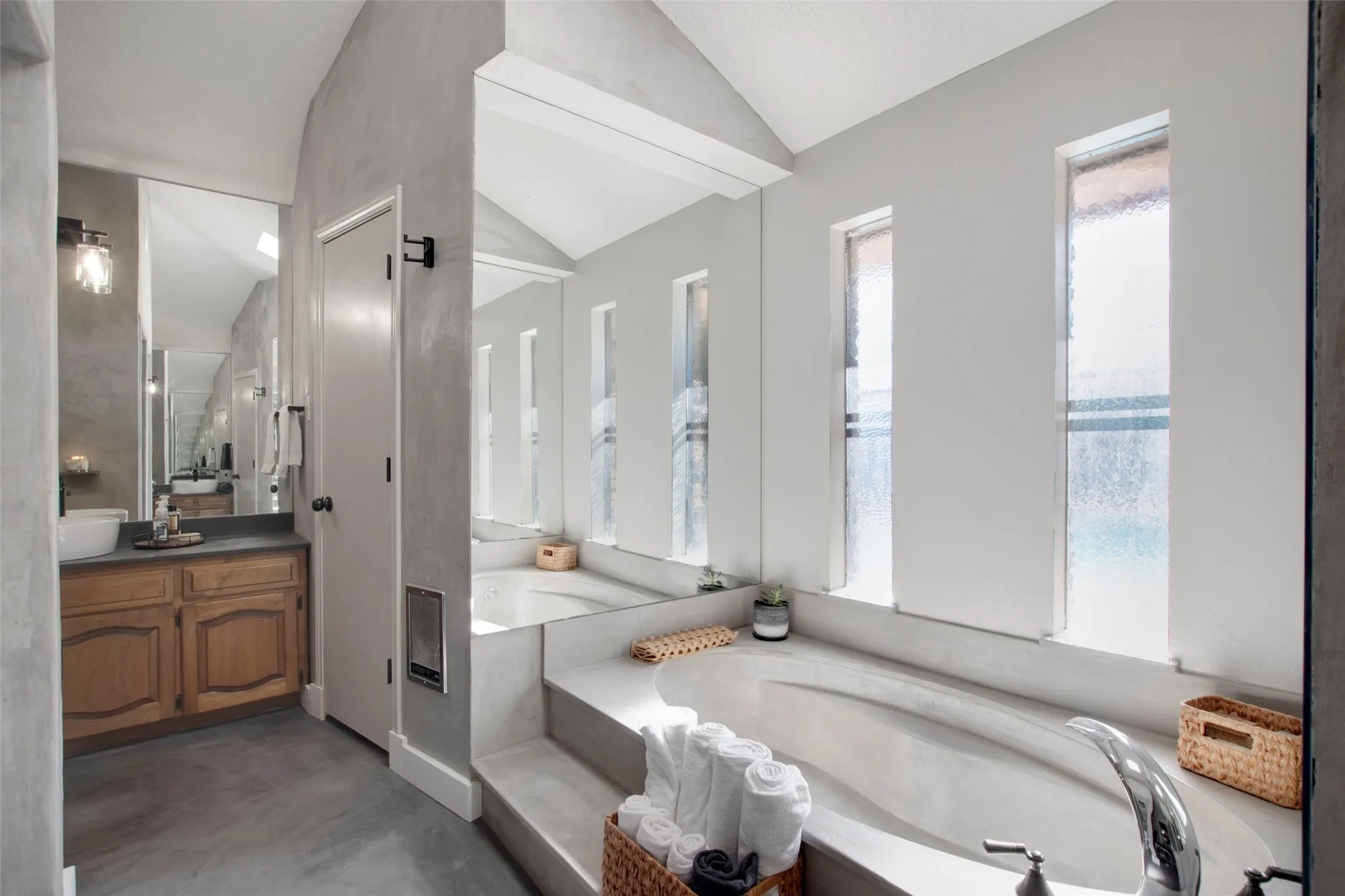 Bathroom with concrete flooring, vanity, a bathtub, and vaulted ceiling