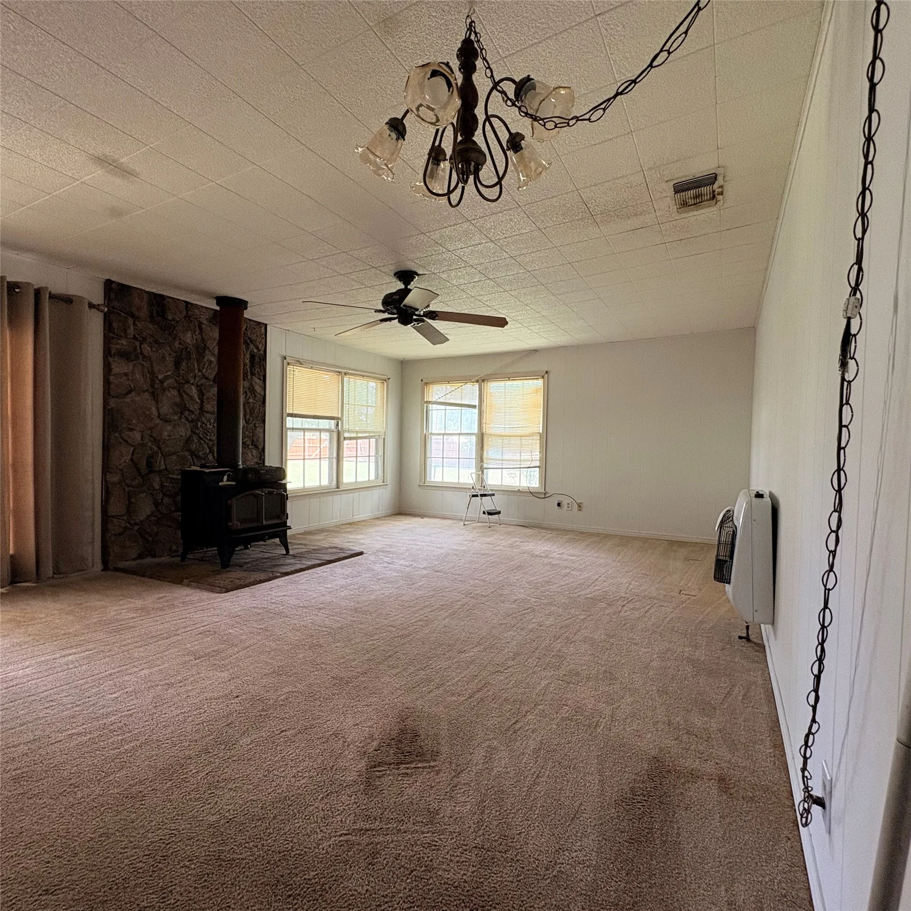 Spacious room featuring a stone-faced wall, a freestanding wood-burning stove, and multiple windows