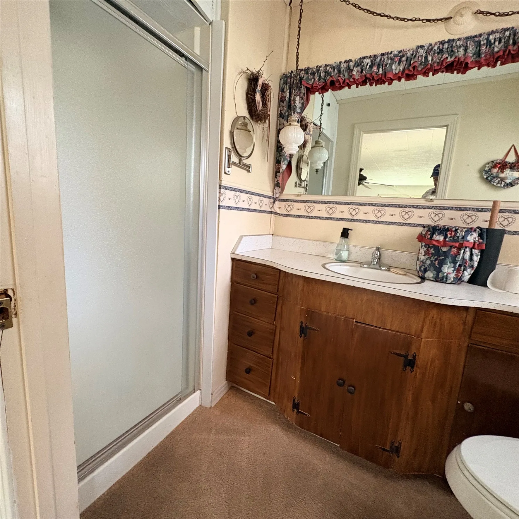 Frosted glass shower enclosure, wood-finish vanity with countertop, built-in sink, wall-mounted mirror, and decorative wall border