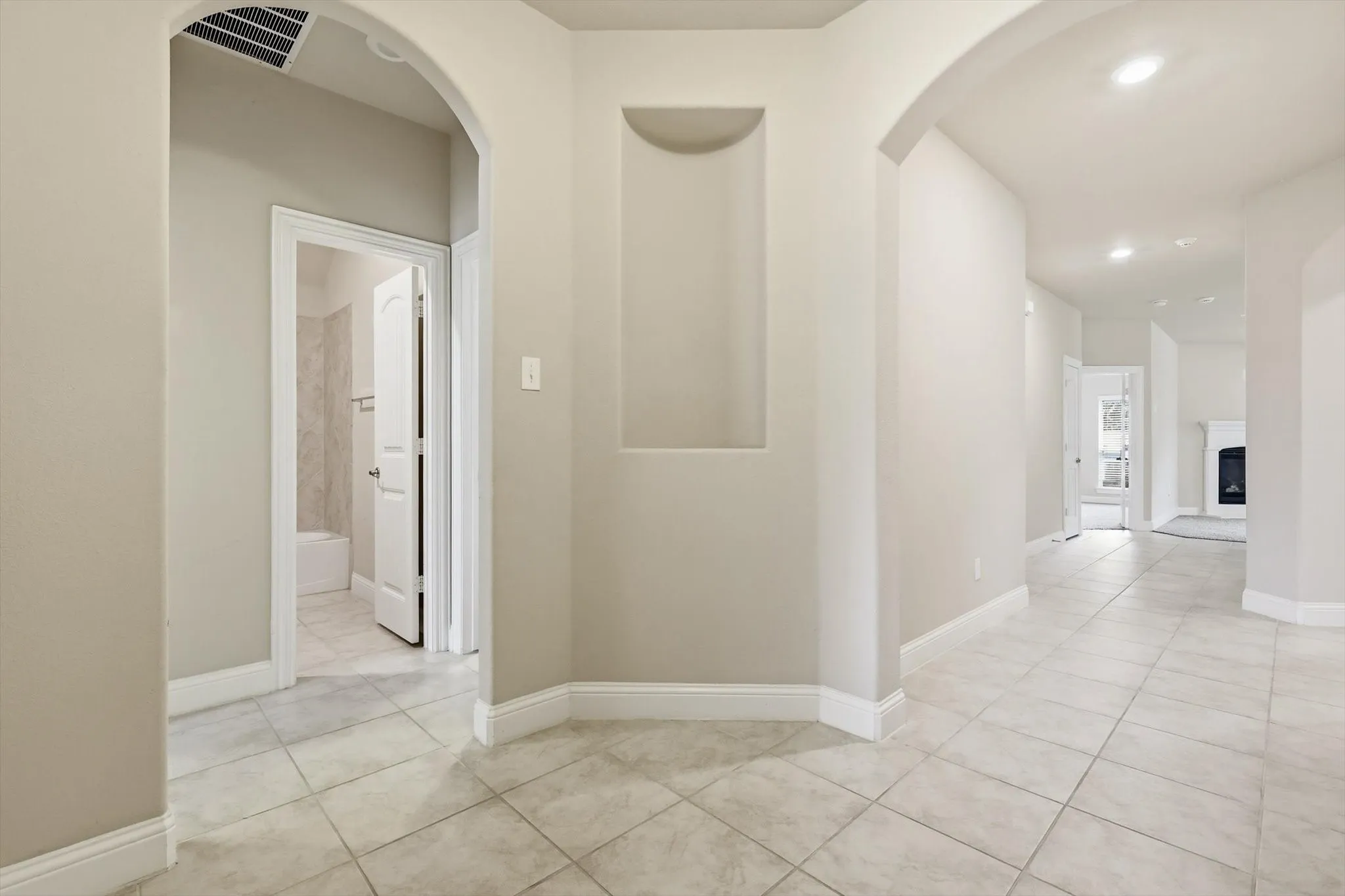 Hallway featuring neutral-toned walls, arched doorways, a built-in wall niche, and tile flooring