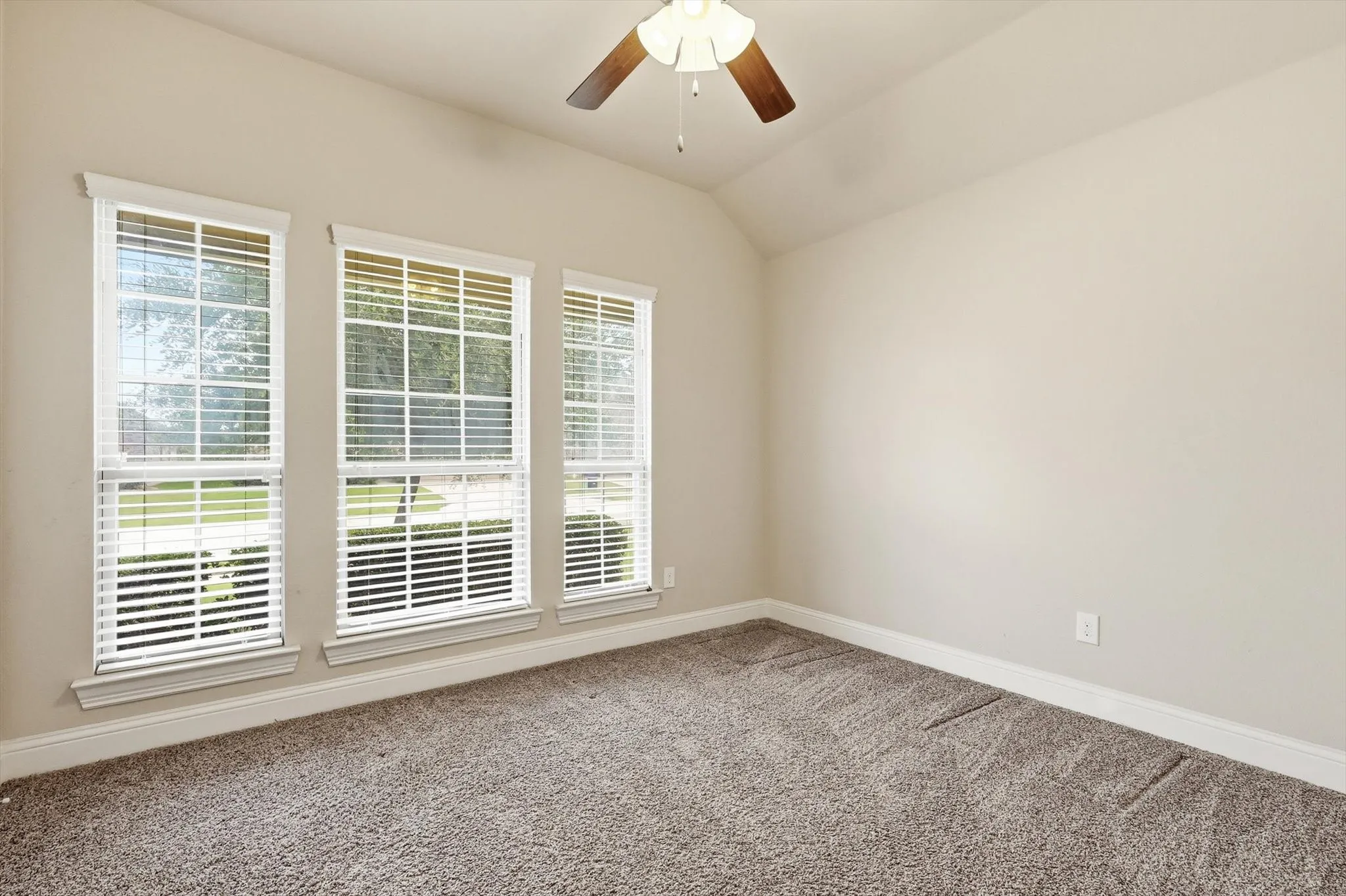 Interior room featuring neutral wall paint, textured carpet flooring, and a ceiling fan with light fixture