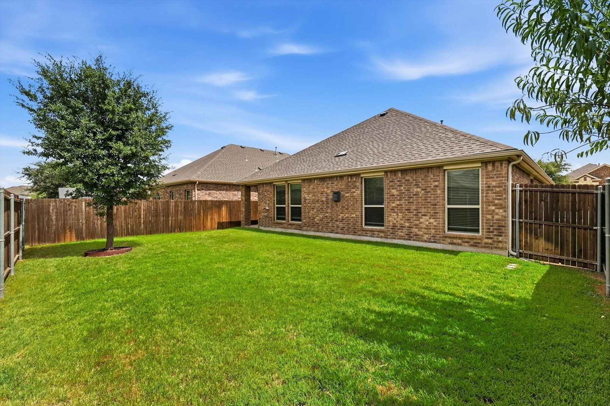 Expansive backyard featuring a lush lawn, mature tree, and full privacy fencing
