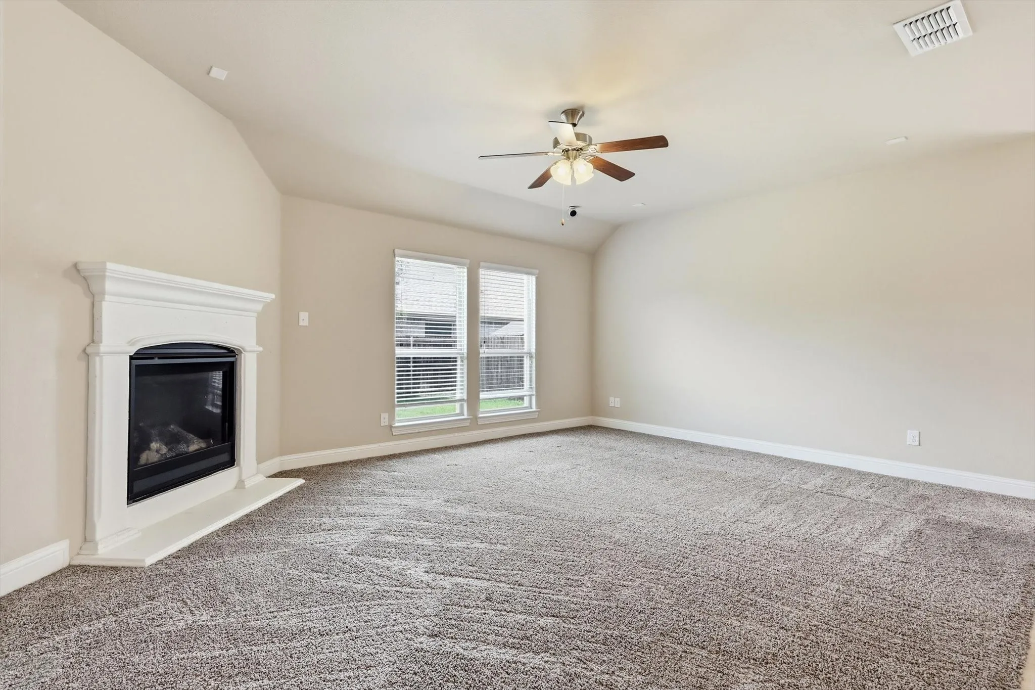 Spacious interior featuring a decorative fireplace with a white mantel, textured carpet flooring, and vaulted ceilings
