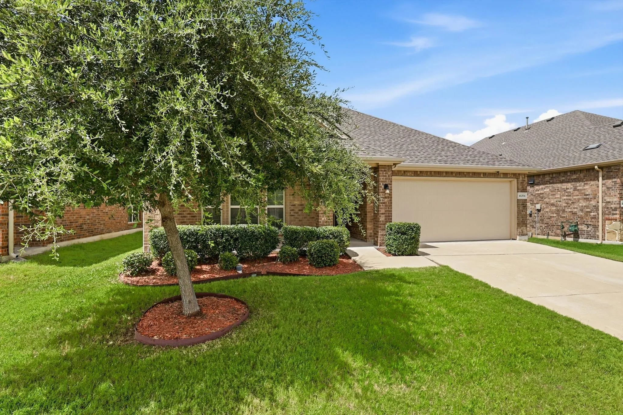 Brick exterior with a two-car garage, concrete driveway, and a manicured lawn