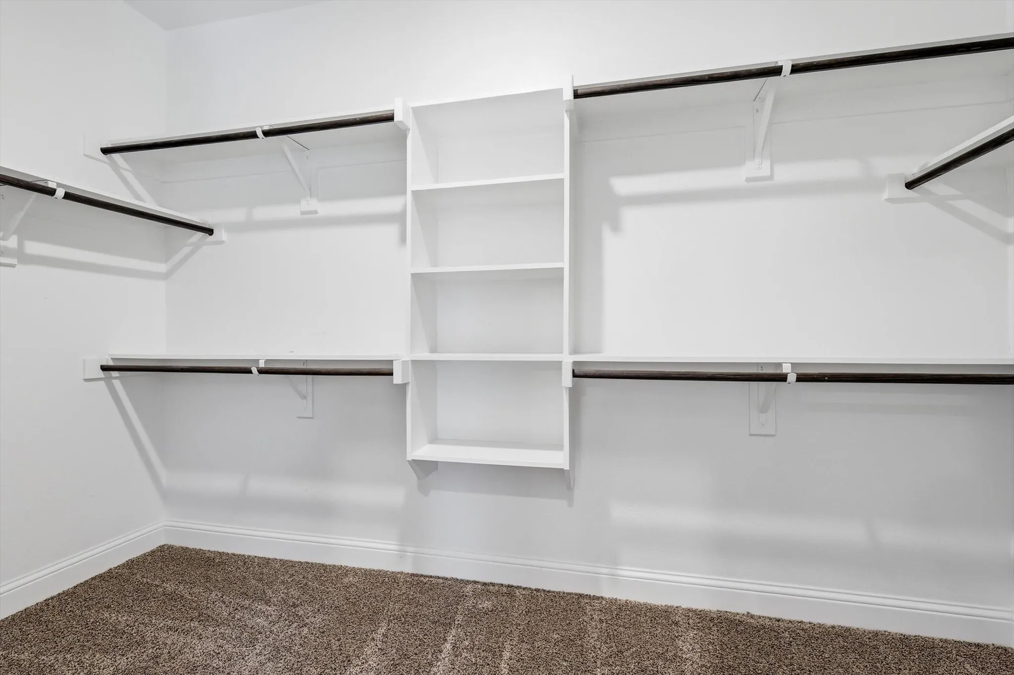 Walk-in closet featuring built-in shelving, multiple hanging rods, white walls, white baseboards, and carpet flooring