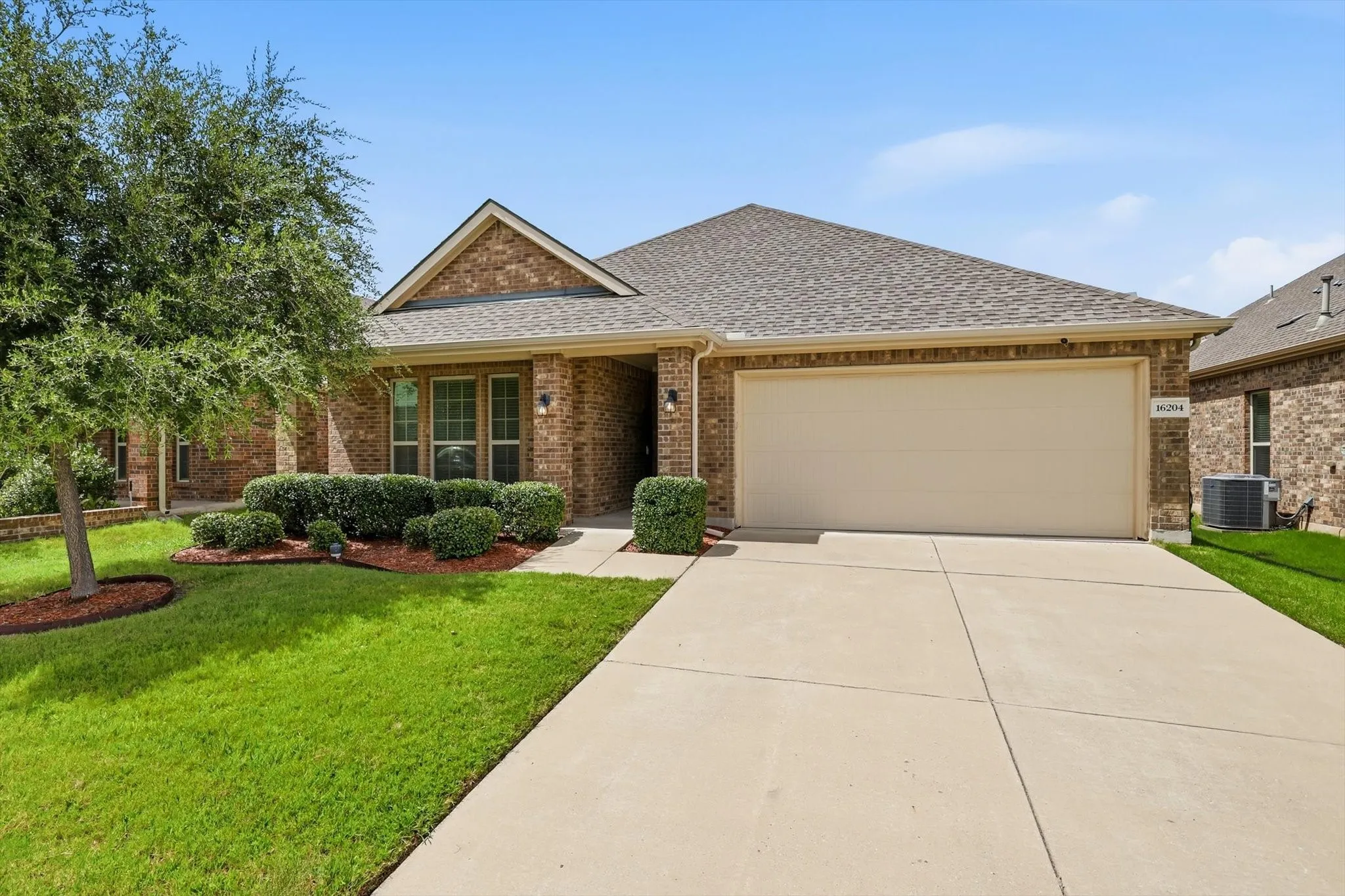 Brick exterior home featuring a gabled roofline, mature landscaping, a concrete driveway, and an attached garage
