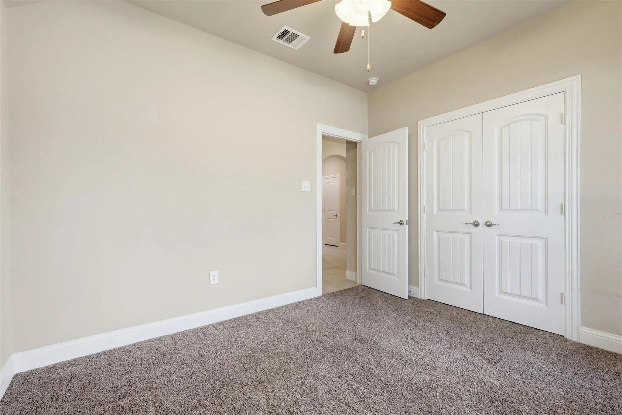 Bedroom featuring neutral wall paint, textured carpeting, a ceiling fan with light fixture, and white bi-fold closet doors