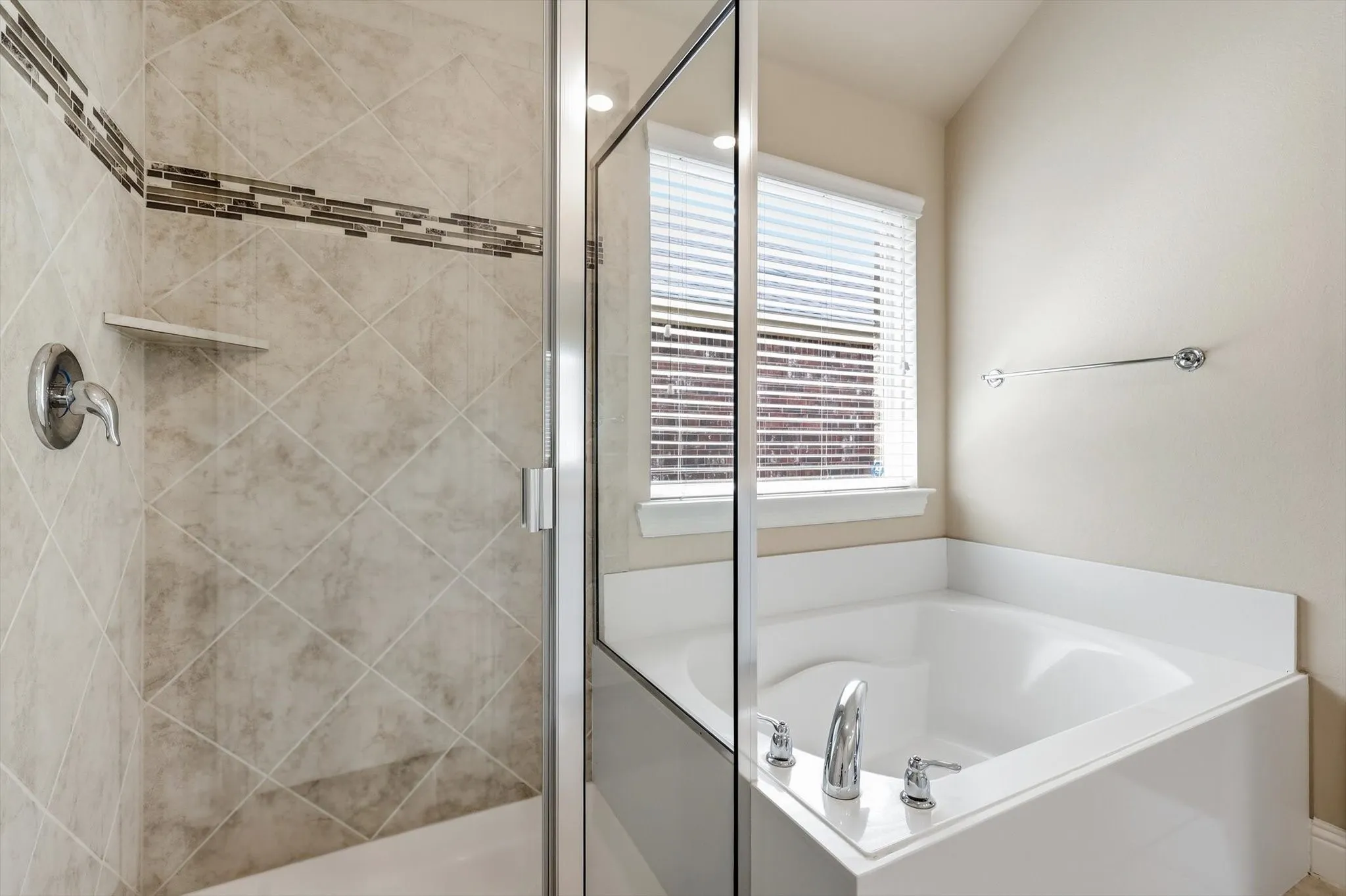 Shower-tub combination featuring a glass enclosure, tiled shower with mosaic accent, built-in shower shelf, and a garden tub with a window above