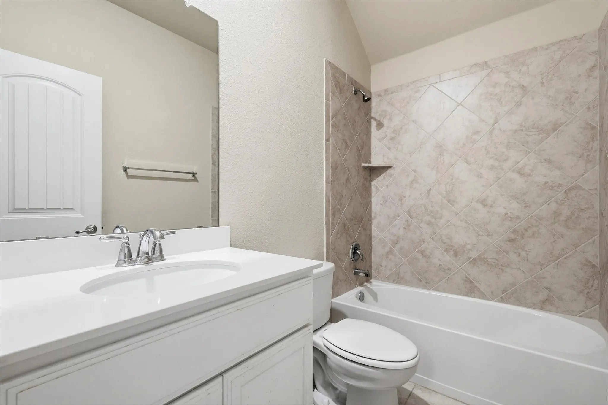 Bathroom featuring a white vanity with an integrated sink, polished chrome faucet, a large wall-mounted mirror, a white toilet, and a bathtub with tile surround
