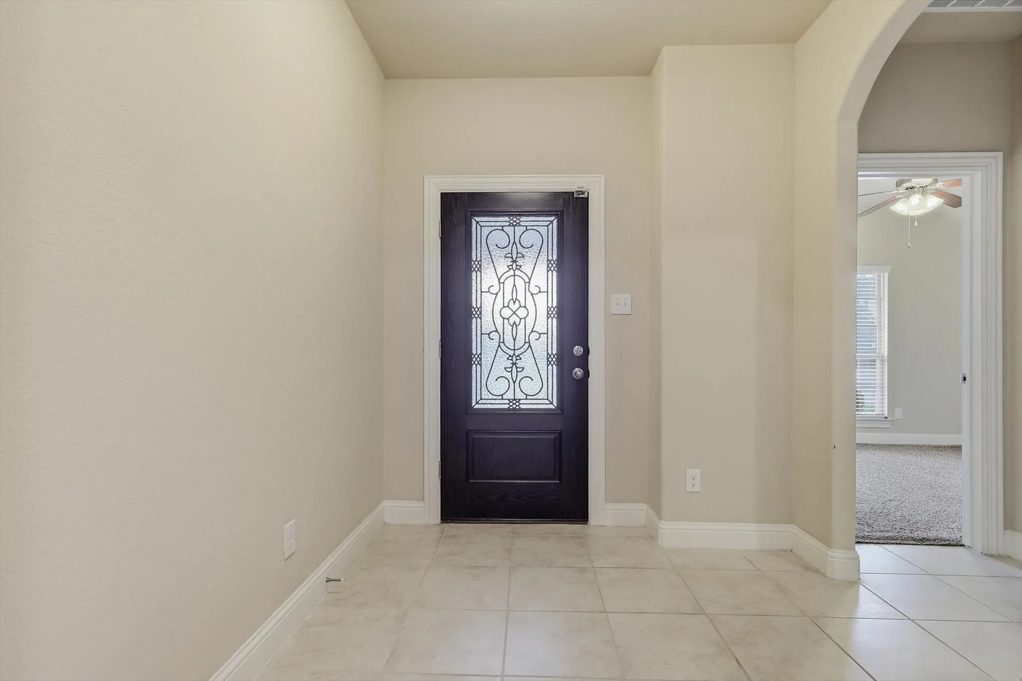 Foyer featuring a dark wood entry door with decorative glass inserts, neutral tile flooring, light beige wall paint, and white baseboards