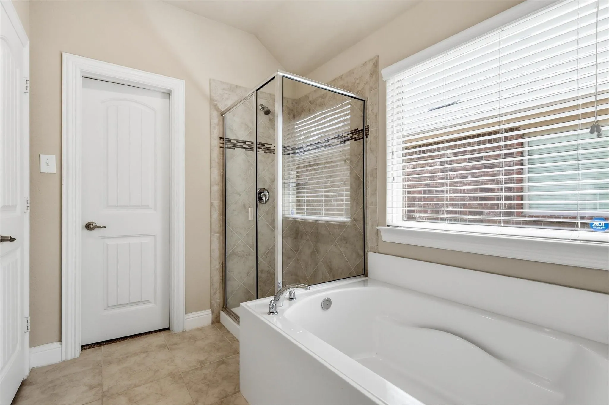 Bathroom featuring a built-in soaking tub with chrome fixtures, a glass-enclosed shower with tiled walls and decorative banding, and large format tile flooring