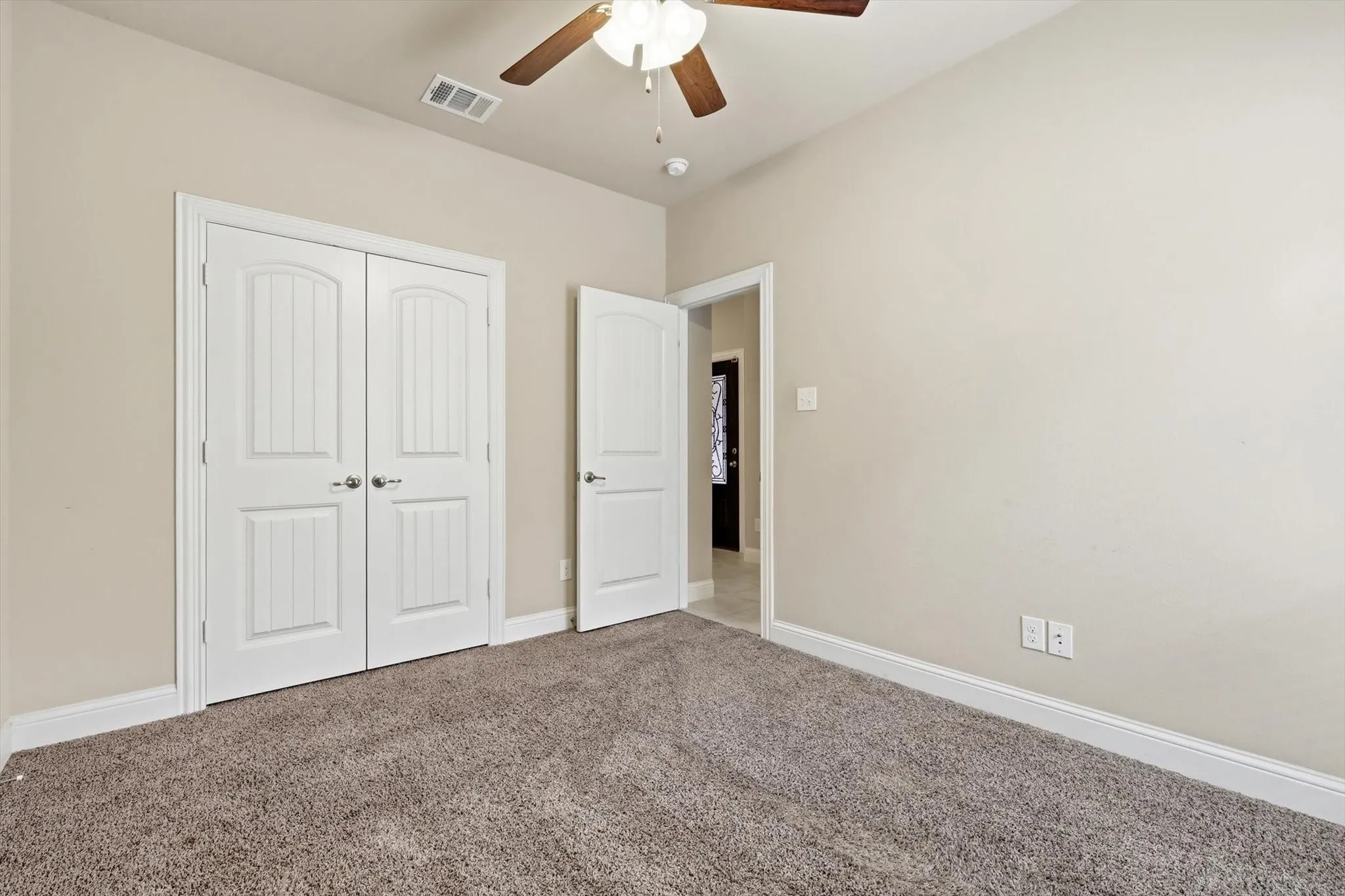 Neutral wall paint with white trim, gray carpet flooring, wood-finish ceiling fan, and white paneled bi-fold doors