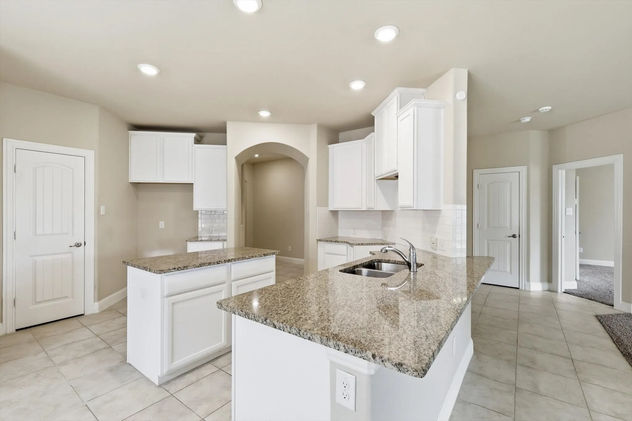 Kitchen featuring dual islands with granite countertops, white cabinetry, a double basin sink, recessed lighting, and tile flooring