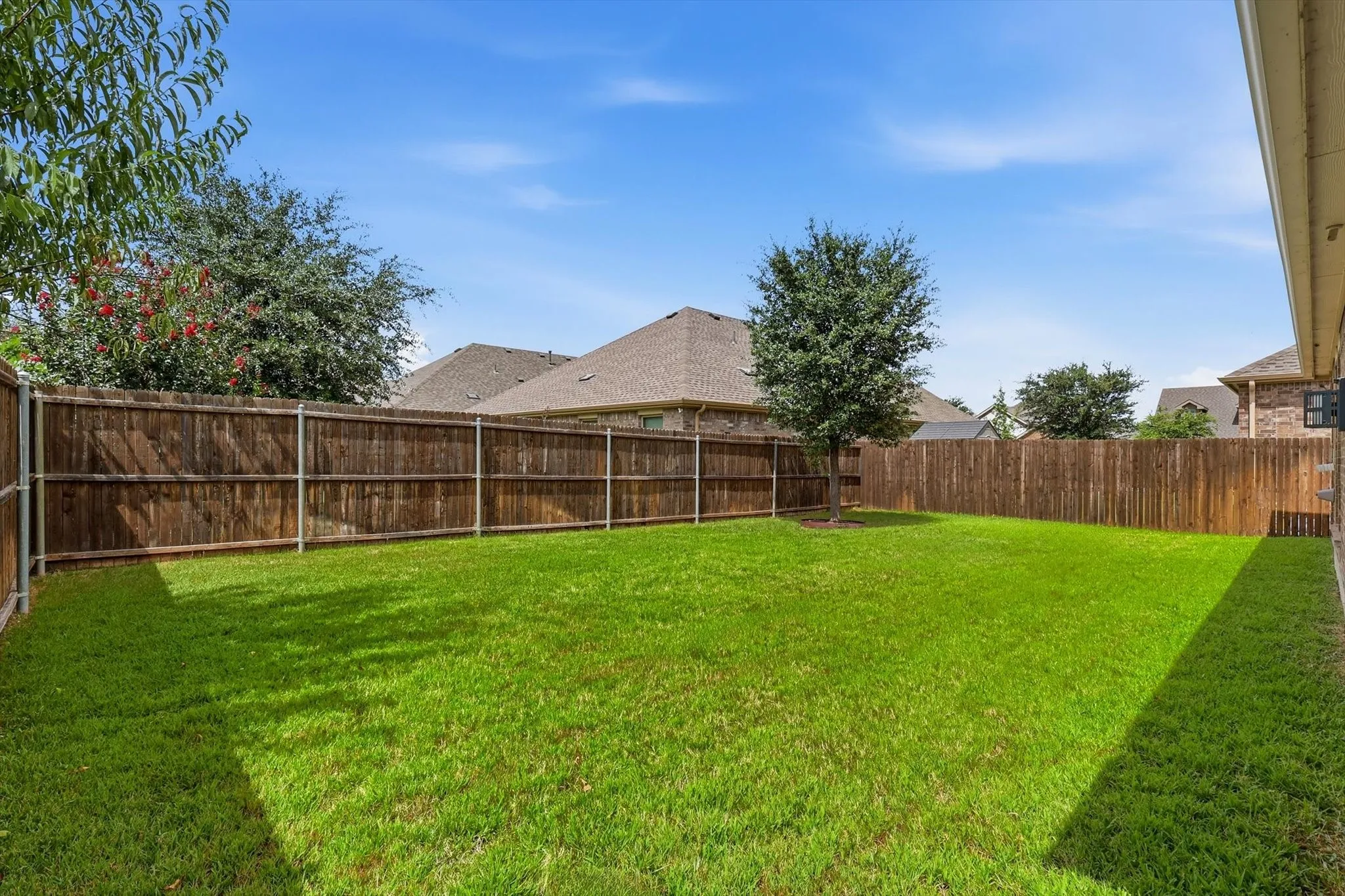 Expansive backyard featuring a manicured lawn, established perimeter fencing, and mature trees