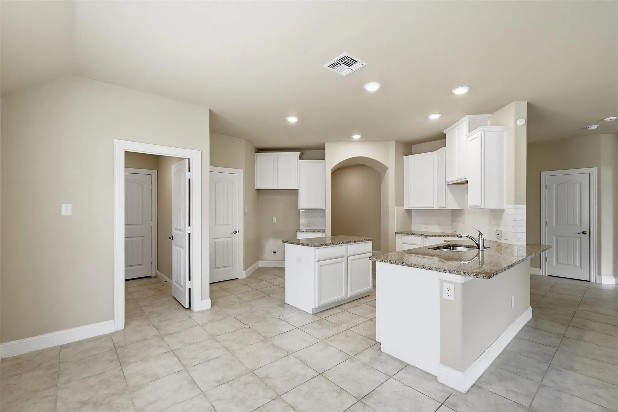 Open-concept kitchen featuring two islands, white cabinetry, granite countertops, and tile flooring