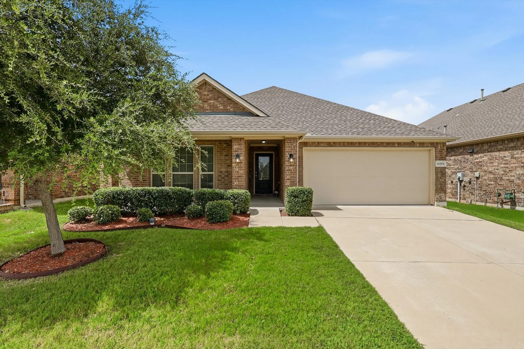 Brick exterior with an attached garage, featuring a concrete driveway, established landscaping, and a covered entry