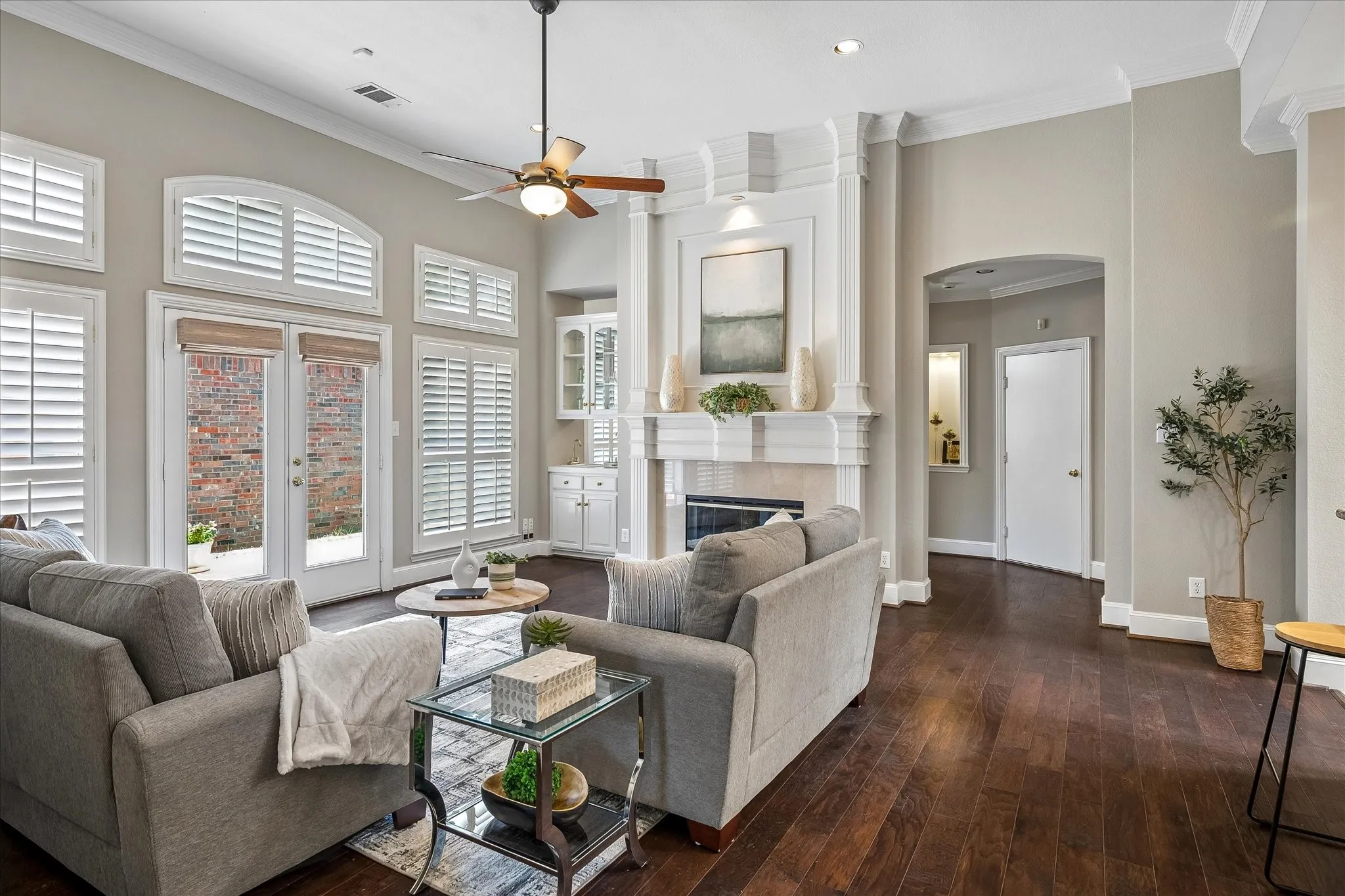 Family room with amazing crown moldings, wet bar, fireplace, wood flooring and beautiful shutters.
