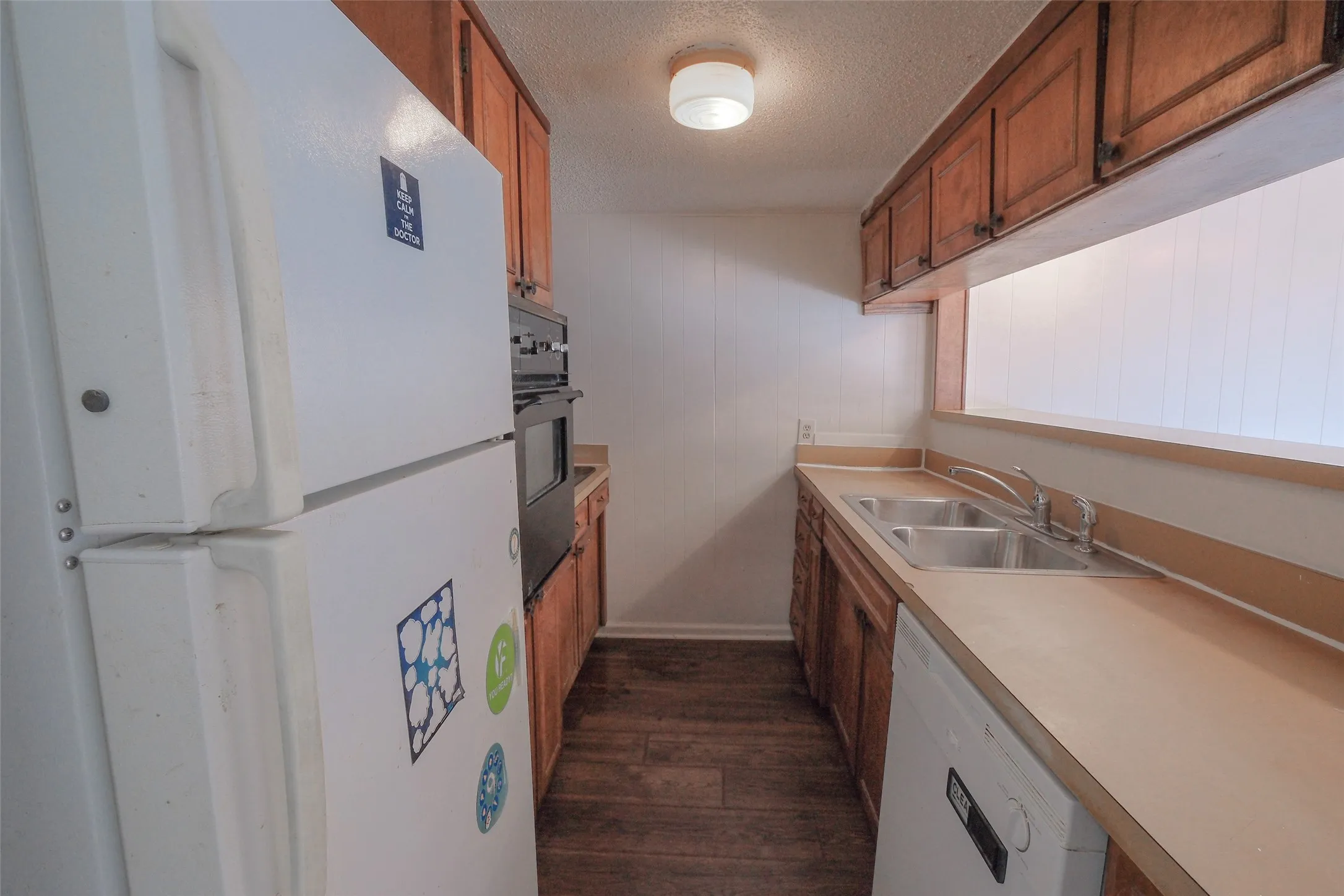 Kitchen featuring wood-finish flooring, wood cabinetry, a dual-basin stainless steel sink, and a built-in oven