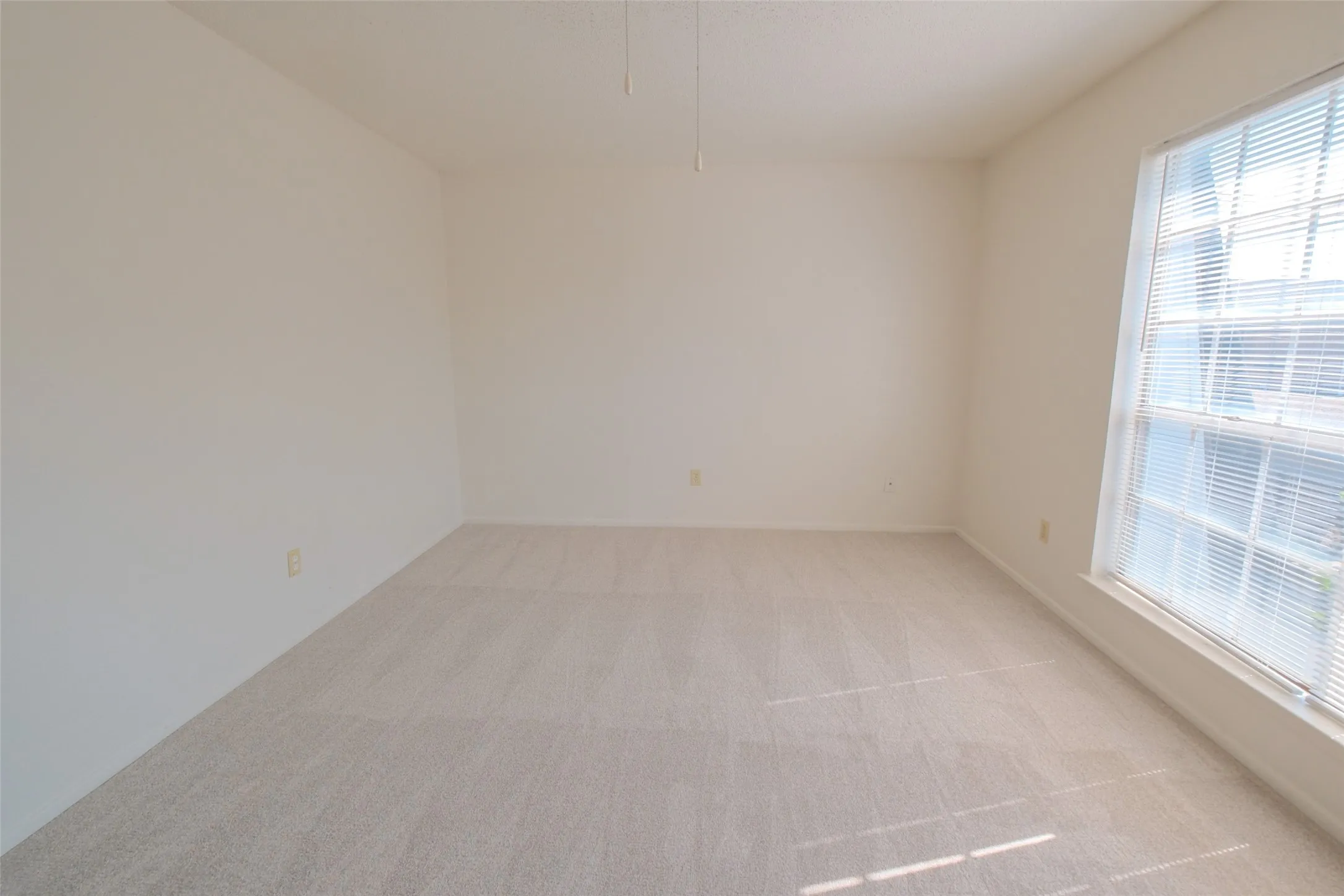 Neutral-toned room featuring a large window with horizontal blinds, light-colored carpet, and a ceiling fan