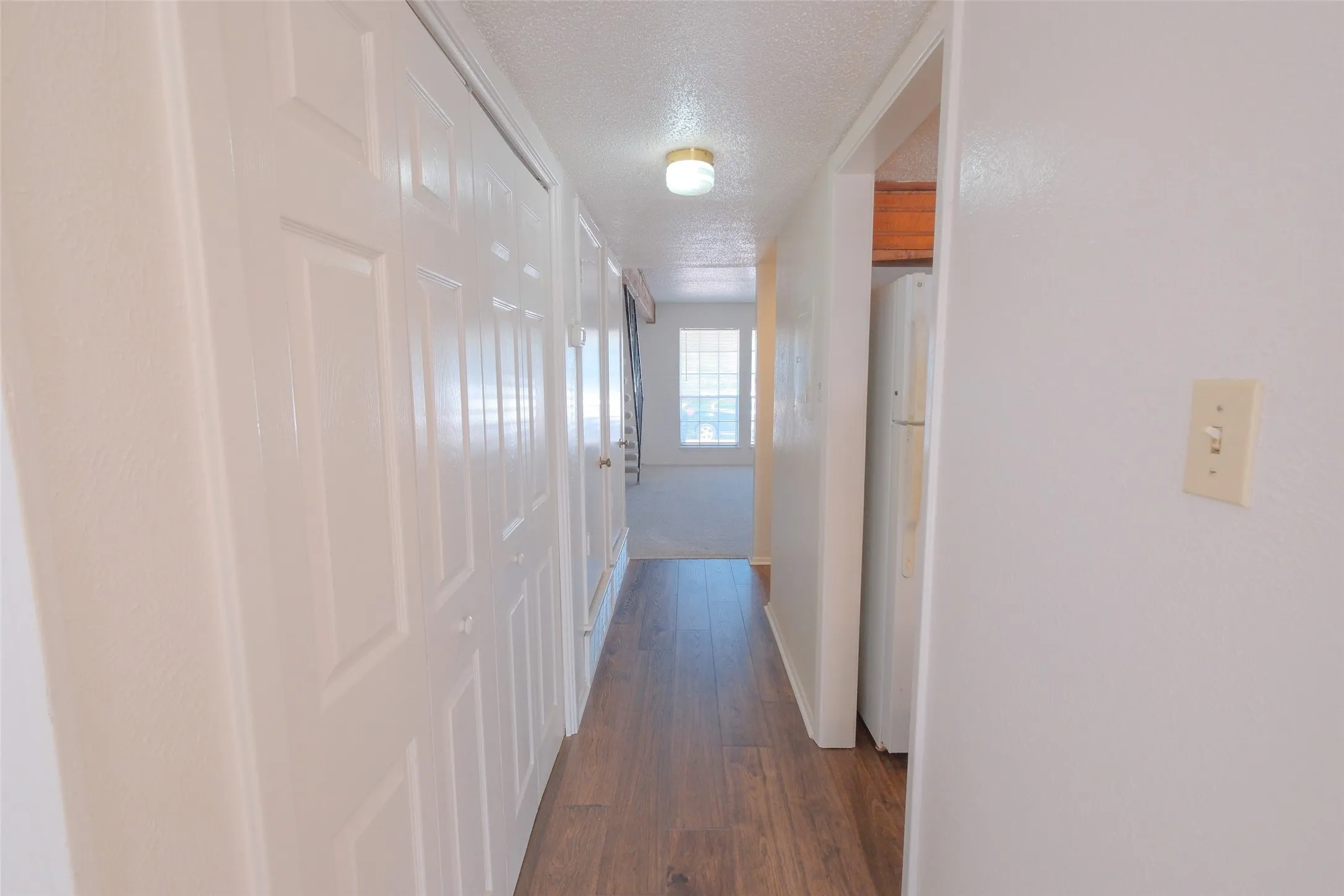 Hallway featuring wood-finish flooring, white paneled bifold closet doors, a flush-mount ceiling light fixture, and white painted walls