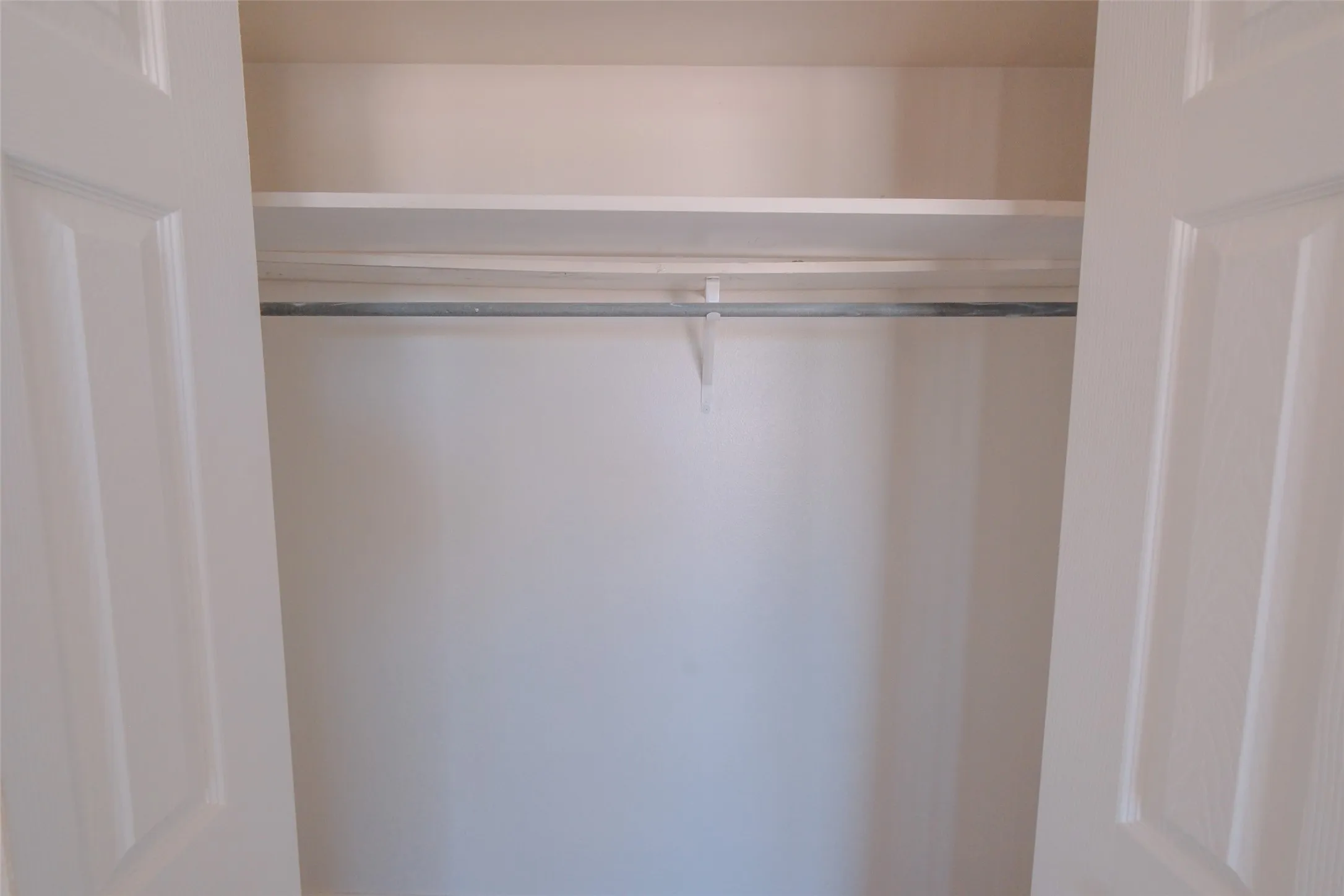 Closet with white paneled bifold doors, integrated shelving, and a metal hanging rod