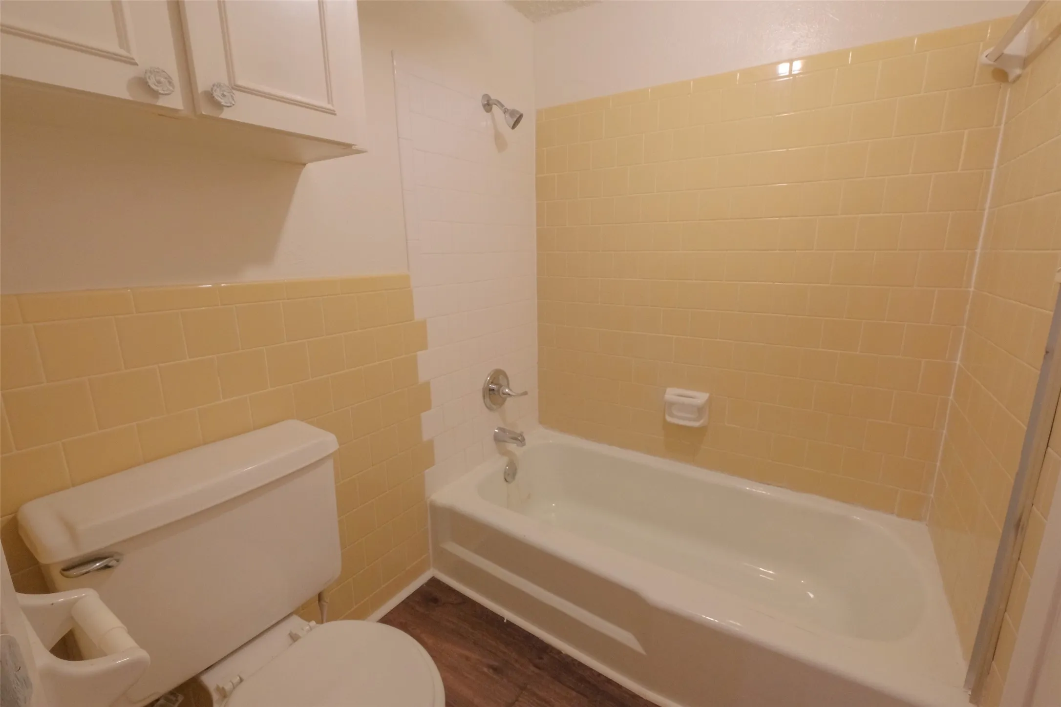 Bathroom featuring a ceramic bathtub, yellow subway tile surround, white wall tile, wood-finish flooring, and white cabinetry with decorative knobs